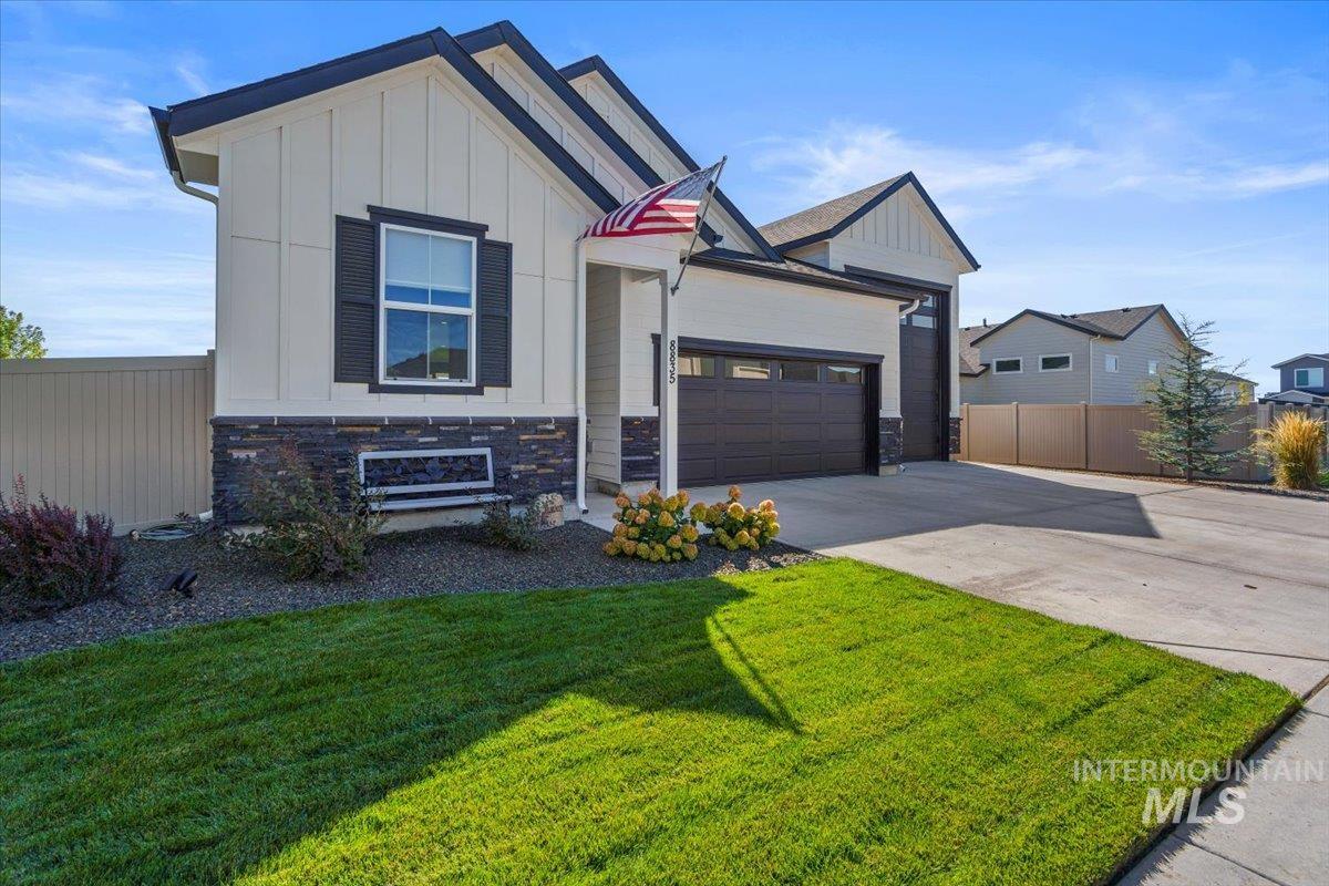 View of front of house with board and batten siding, driveway, stone siding, and an attached garage