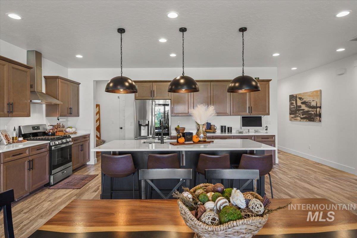 Kitchen with a breakfast bar area, stainless steel appliances, a center island with sink, light wood-type flooring, and decorative light fixtures