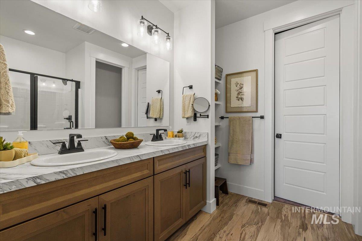 Full bathroom with double vanity, light wood-style floors, and a shower stall