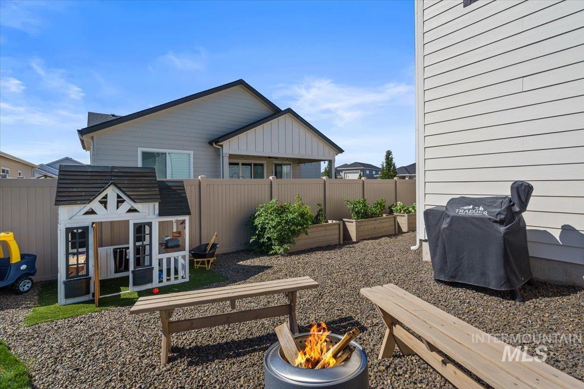 Fenced backyard with a fire pit, a vegetable garden, a grill, and an outdoor structure
