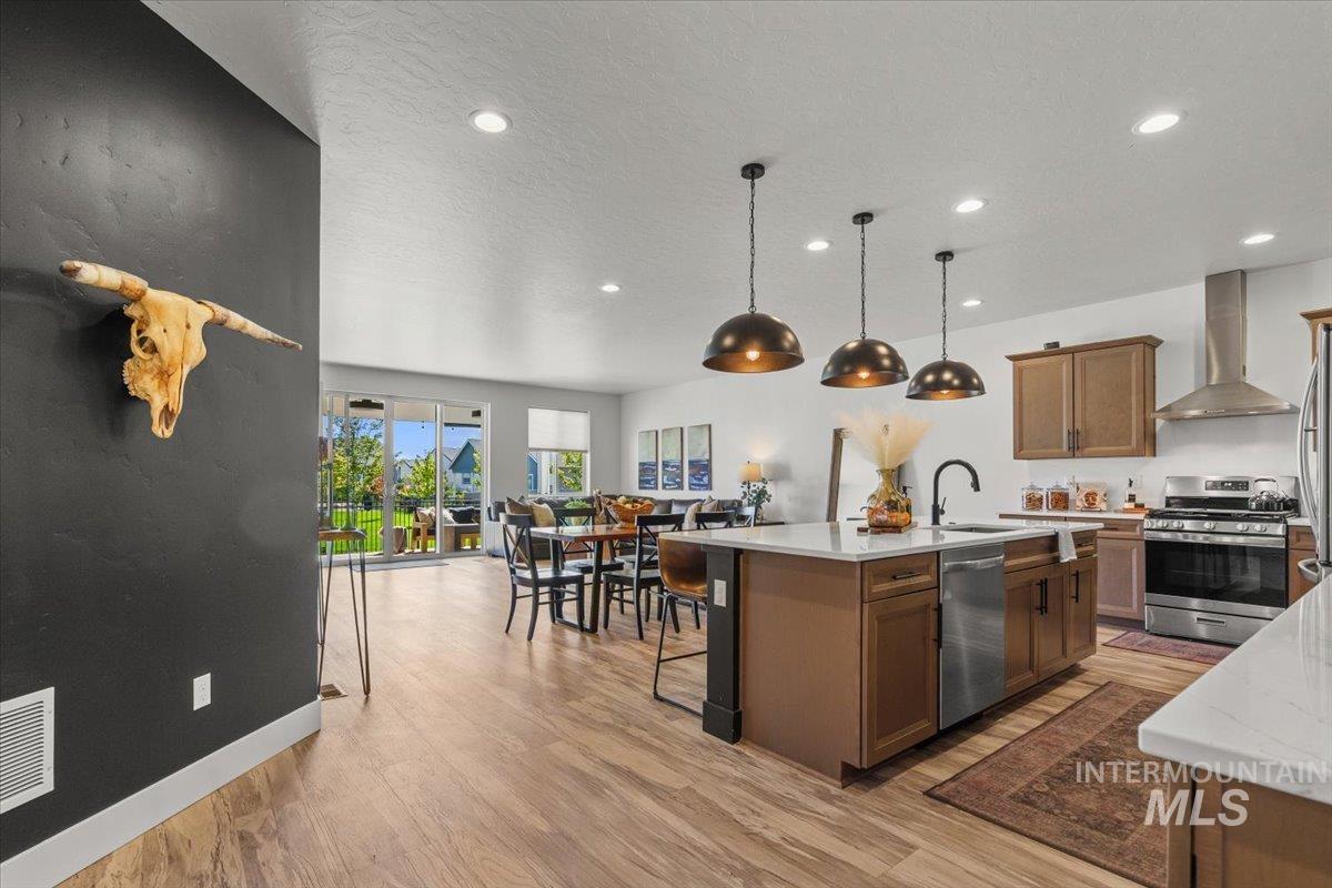 Kitchen with stainless steel appliances, wall chimney exhaust hood, light wood-type flooring, a kitchen bar, and light stone countertops