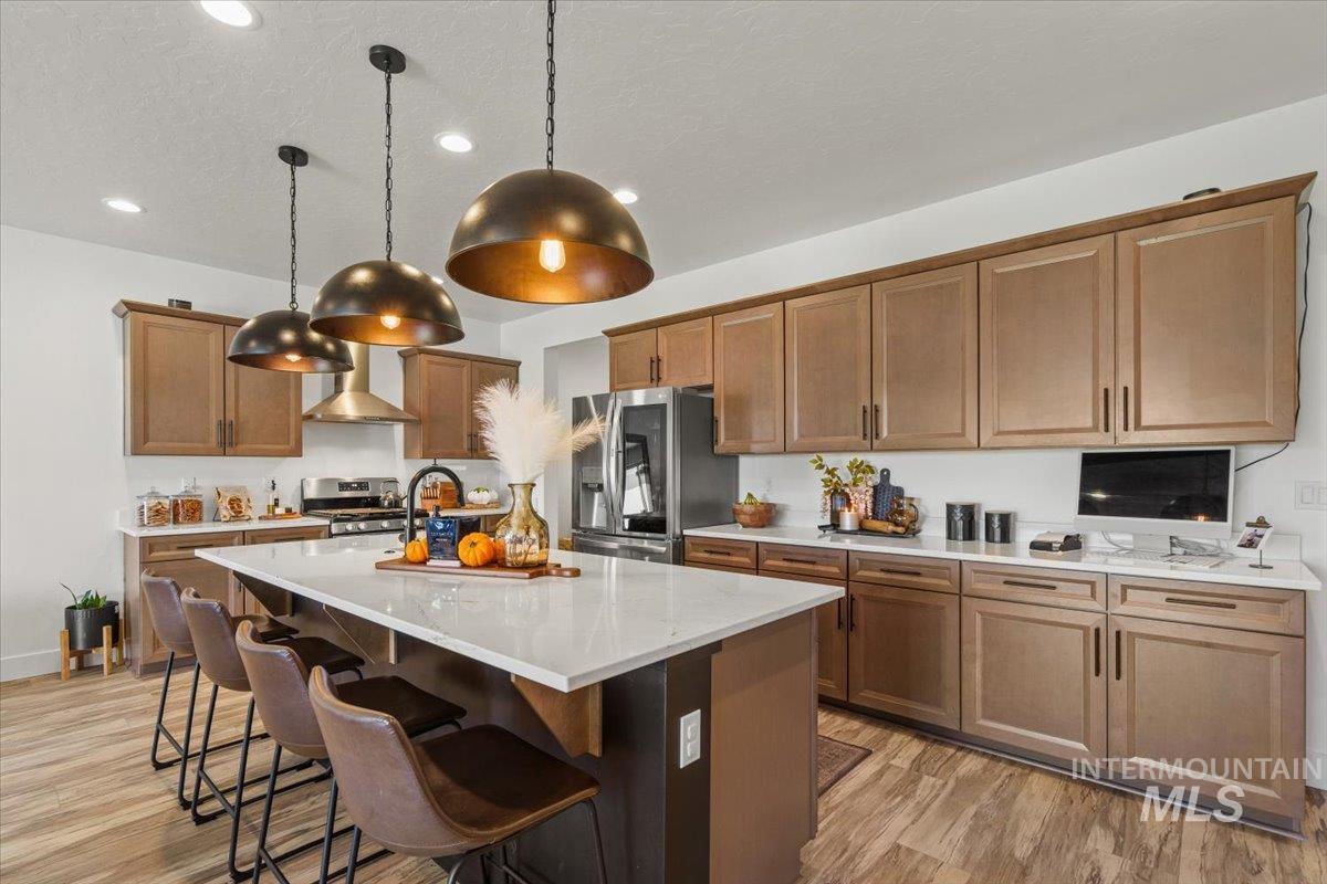 Kitchen featuring a breakfast bar, a center island with sink, light wood finished floors, appliances with stainless steel finishes, and brown cabinetry