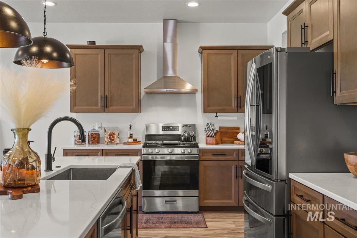 Kitchen with appliances with stainless steel finishes, wall chimney range hood, light wood-style flooring, light stone counters, and recessed lighting