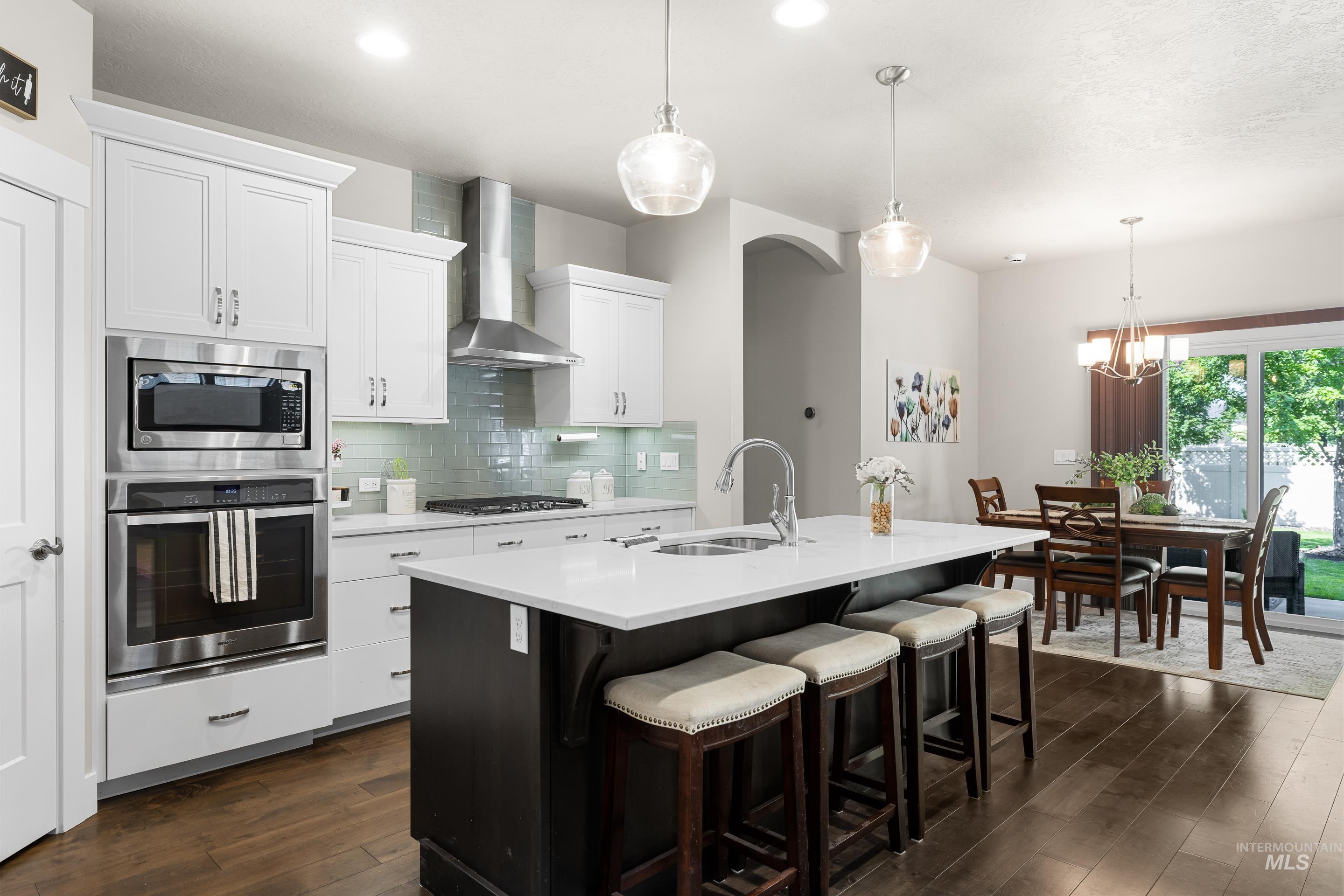 Kitchen featuring stainless steel appliances, tasteful backsplash, wall chimney range hood, light countertops, and a kitchen island with sink