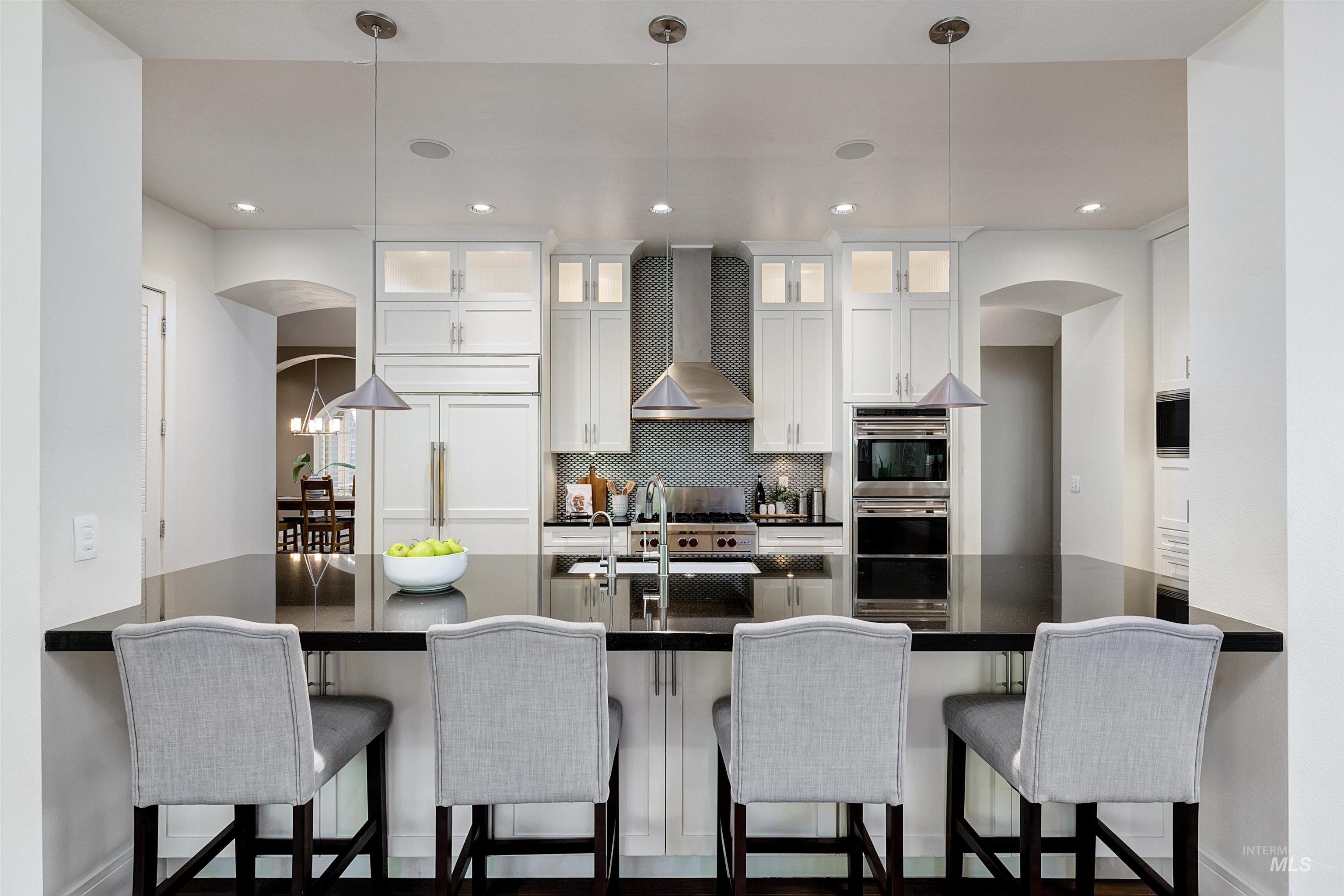 Kitchen with arched walkways, sleek countertop, white shaker cabinets, designer backsplash, and recessed lighting.