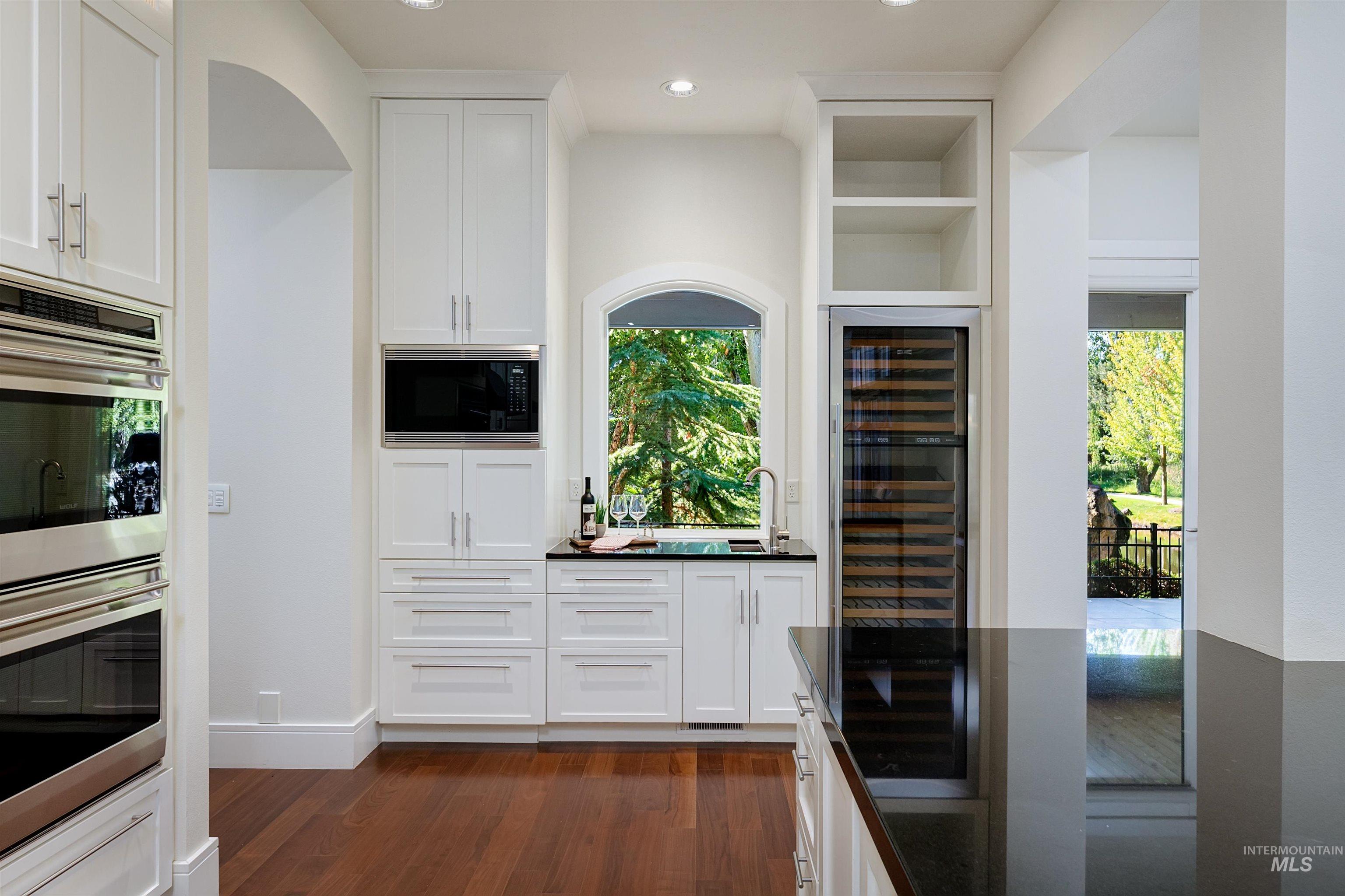 Indoor wet bar featuring full size wine refrigerator, prep sink, plenty of natural light, white cabinetry, dark wood flooring, and recessed lighting.