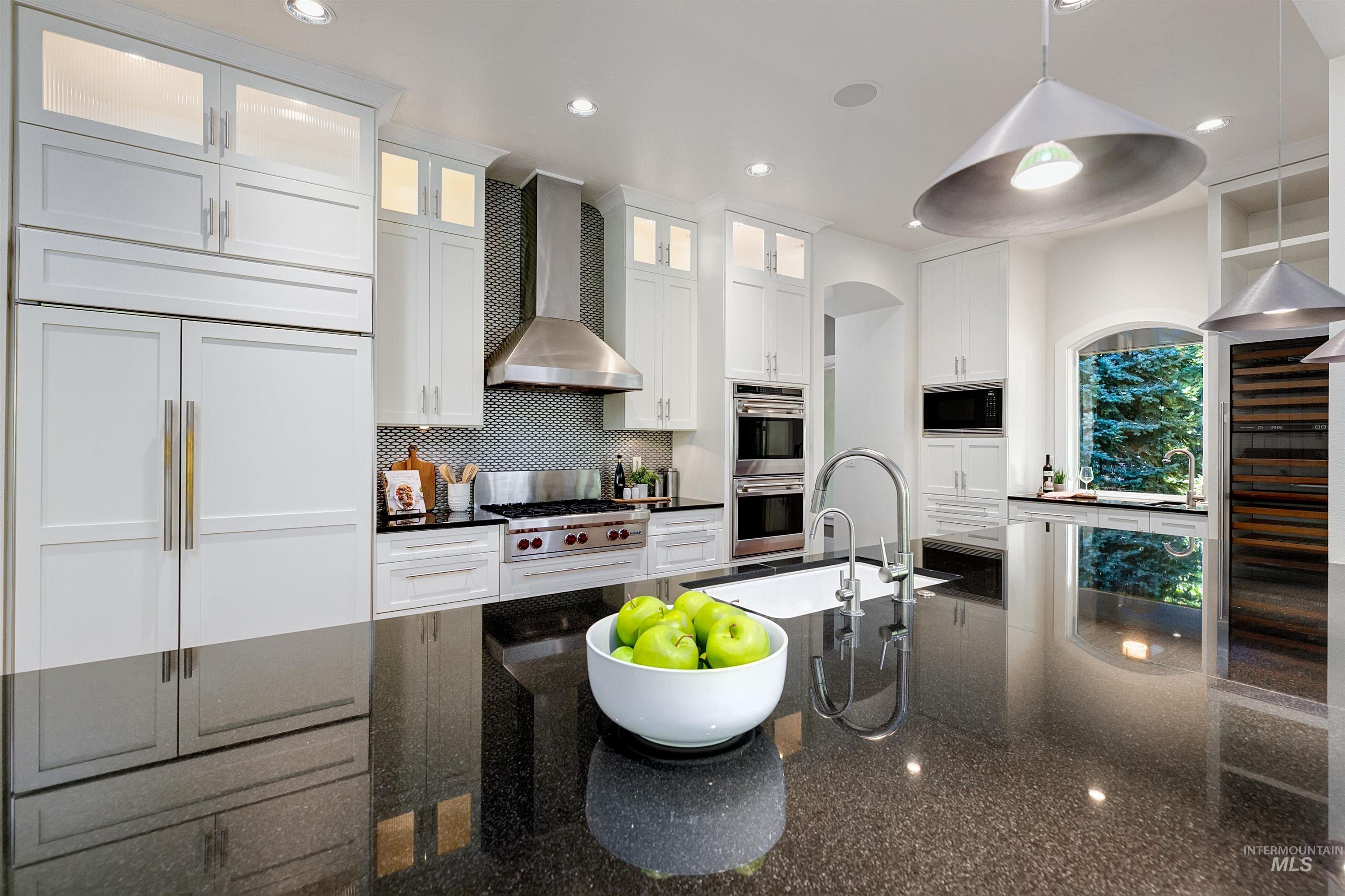 Kitchen with dark stone countertops, designer backsplash, white cabinetry, wall chimney range hood, and recessed lighting.