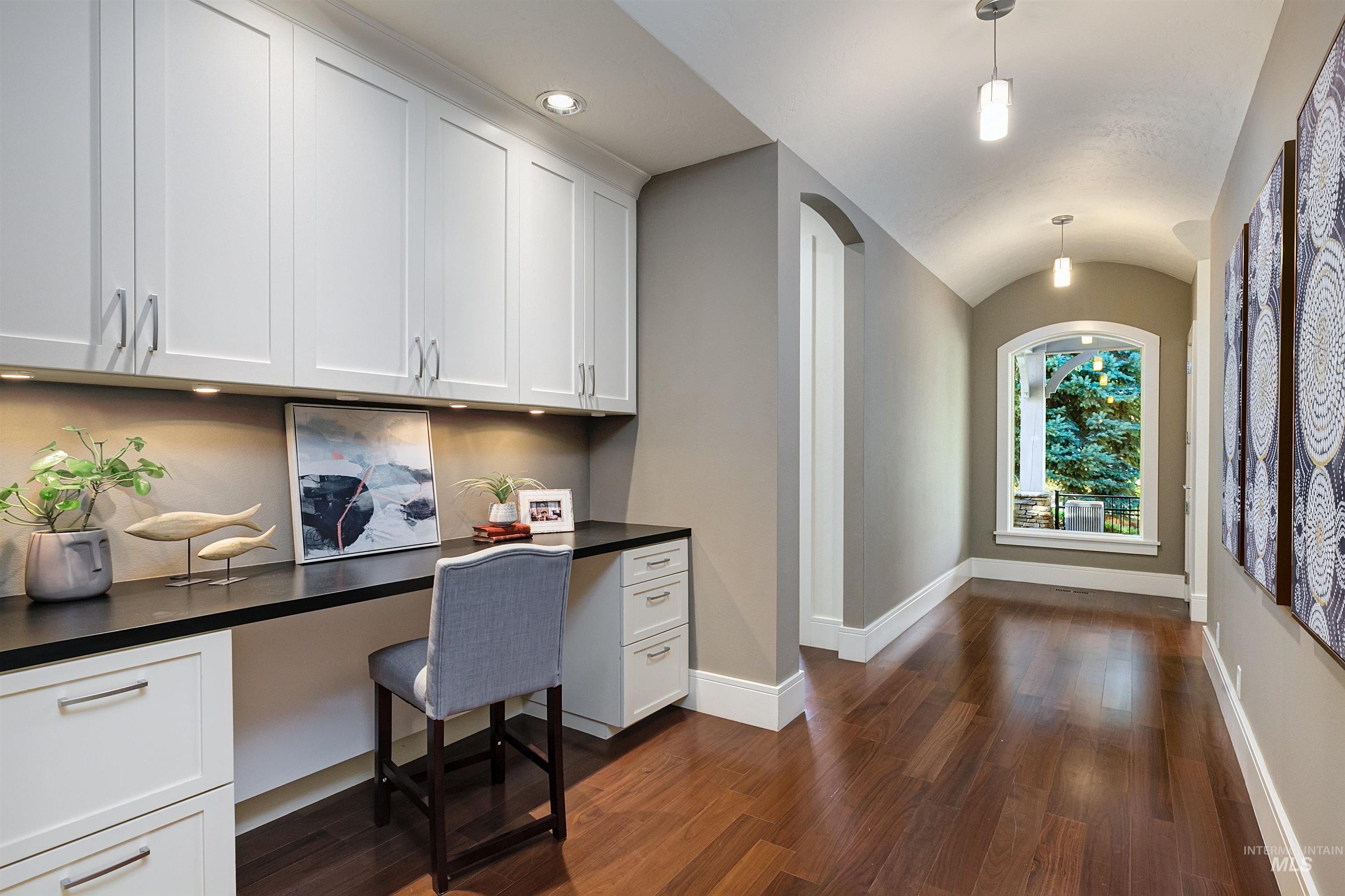 Home office with built in desk, dark wood-style flooring, arched walkways, and vaulted ceiling