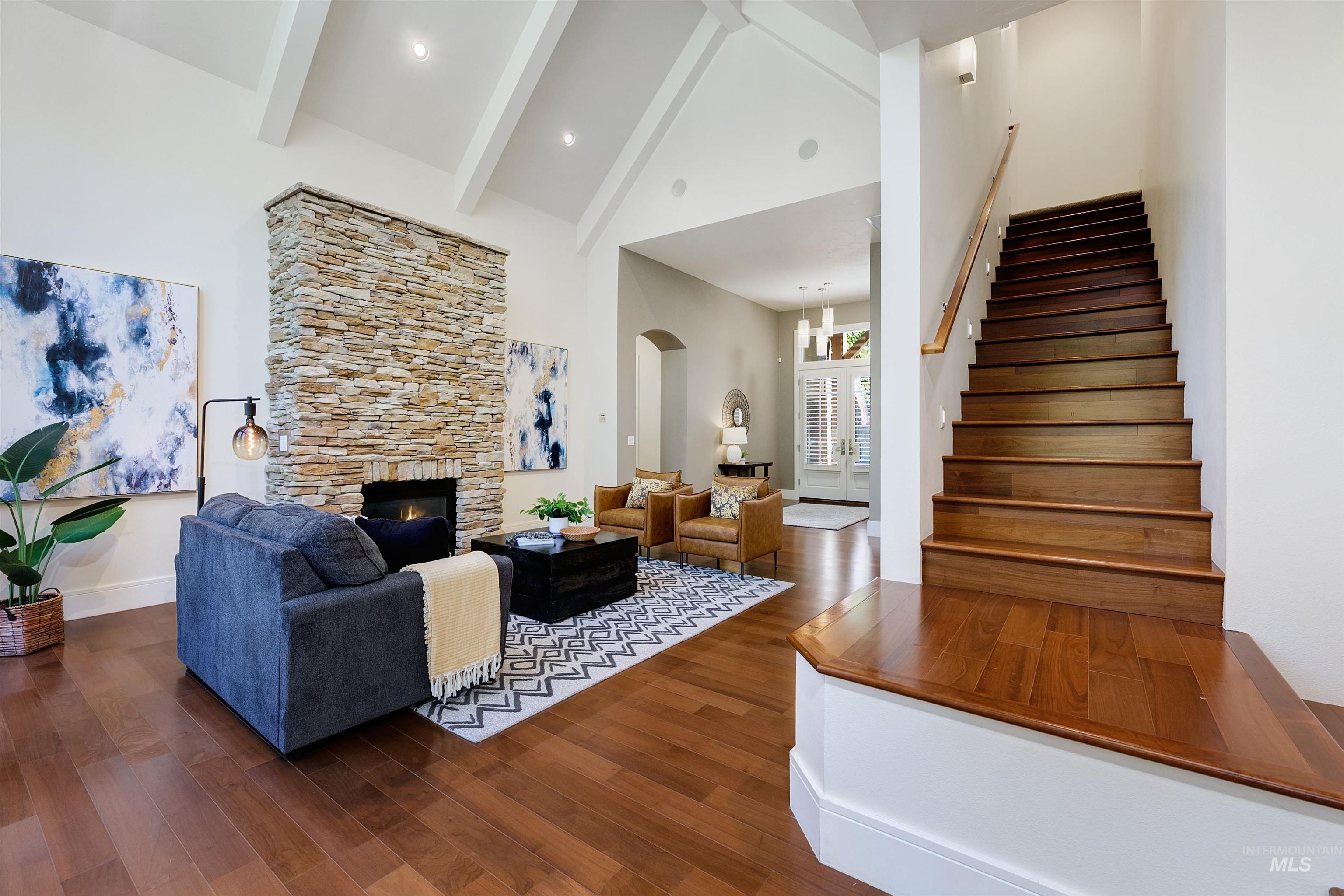 Living room with high vaulted ceiling, dark wood-type flooring, stairs, a stone fireplace, and arched walkways