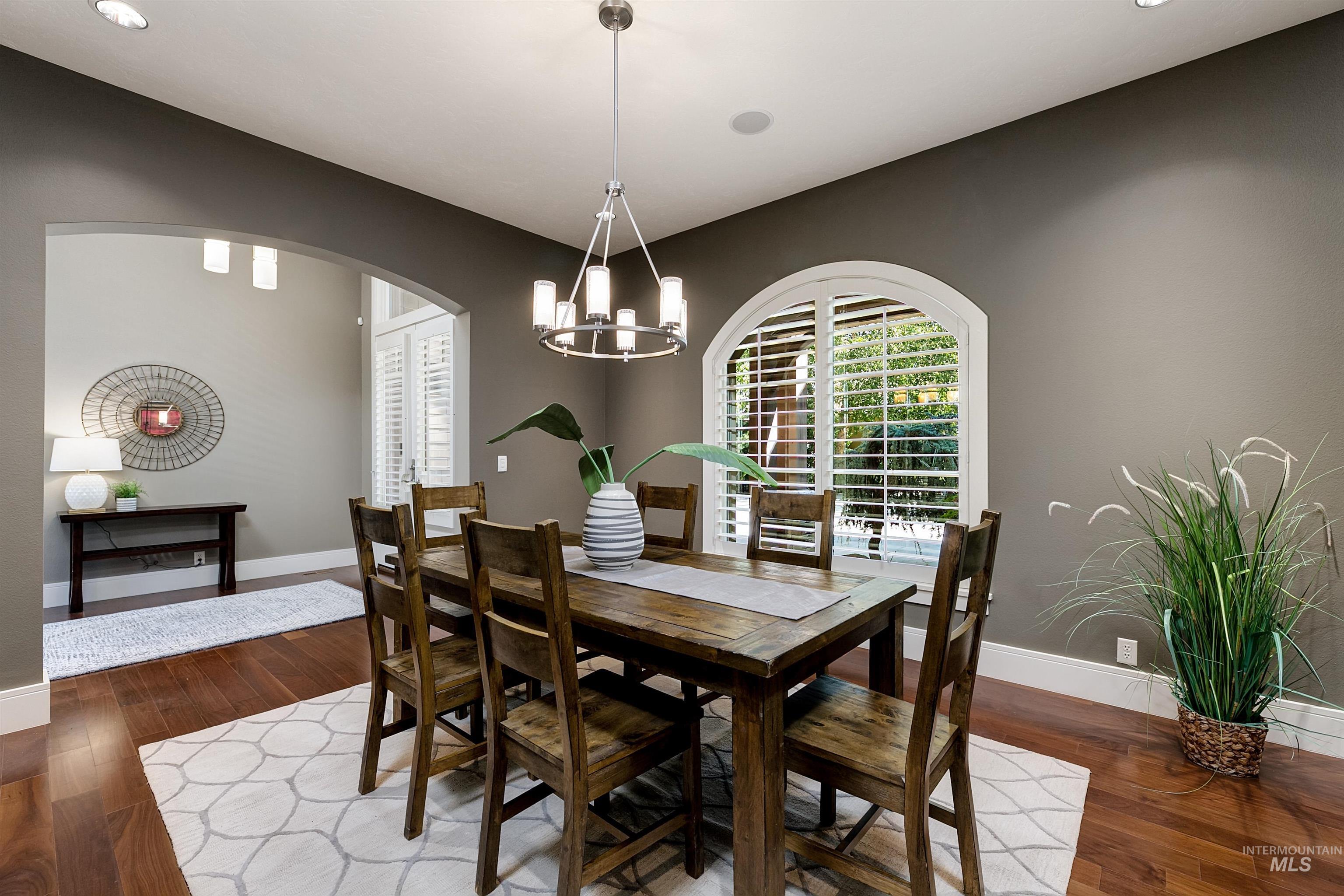 Dining space with dark wood-style floors, a chandelier, arched walkways, and recessed lighting