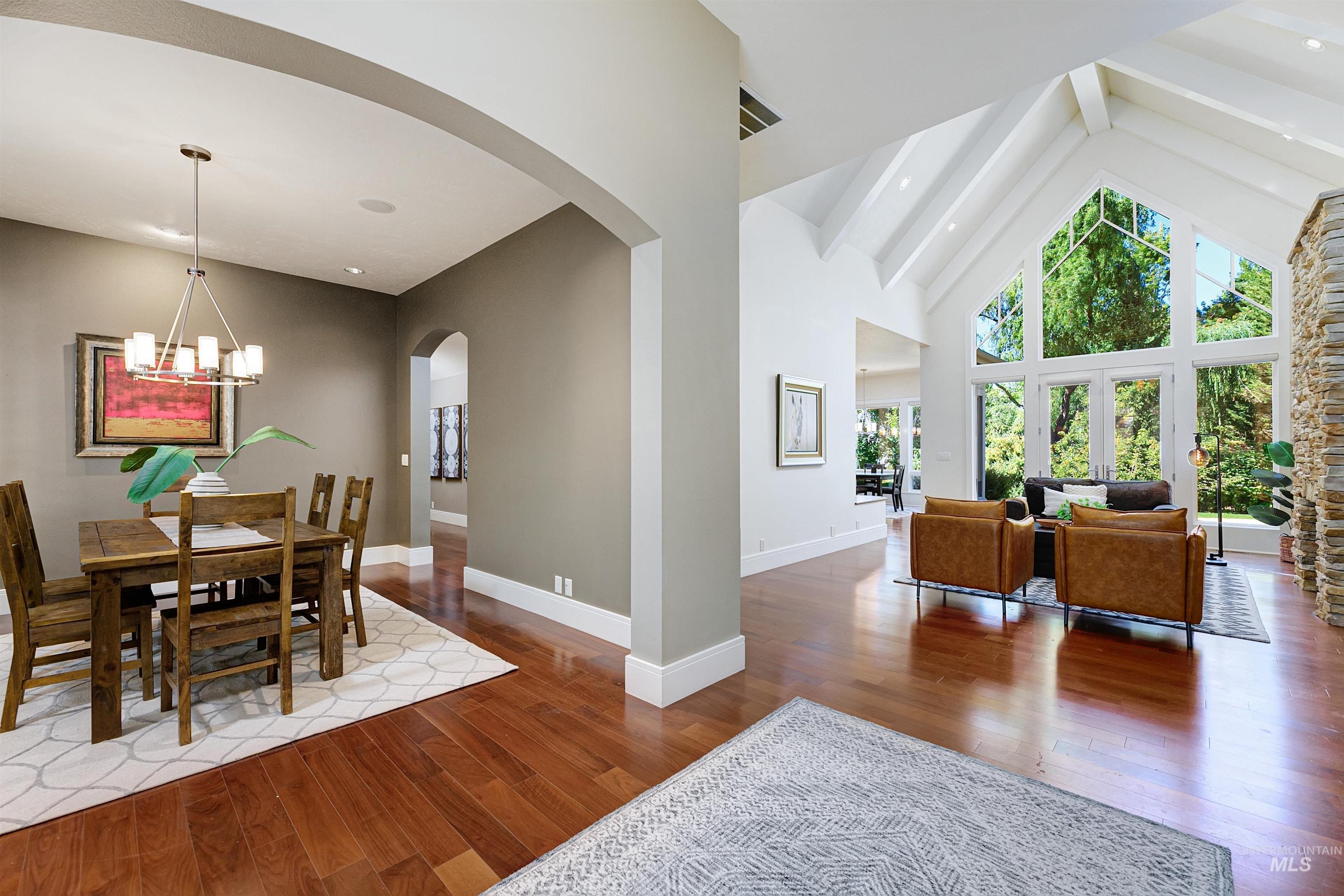 Dining room with elegant light fixture. Adjacent great room with high vaulted ceiling, wood flooring, and array of natural light.