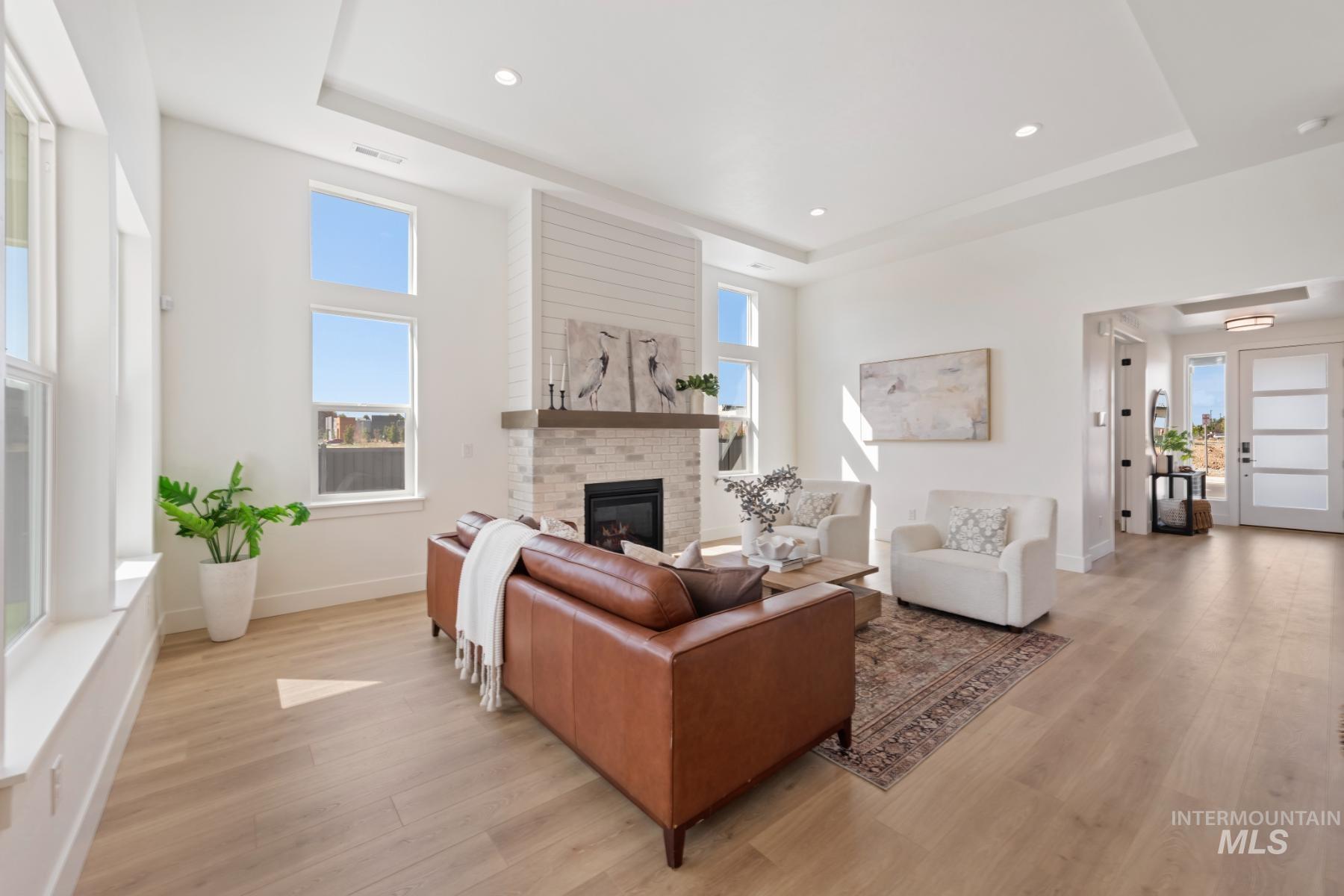 Living room with a tray ceiling, a brick fireplace, light wood-type flooring, and recessed lighting
