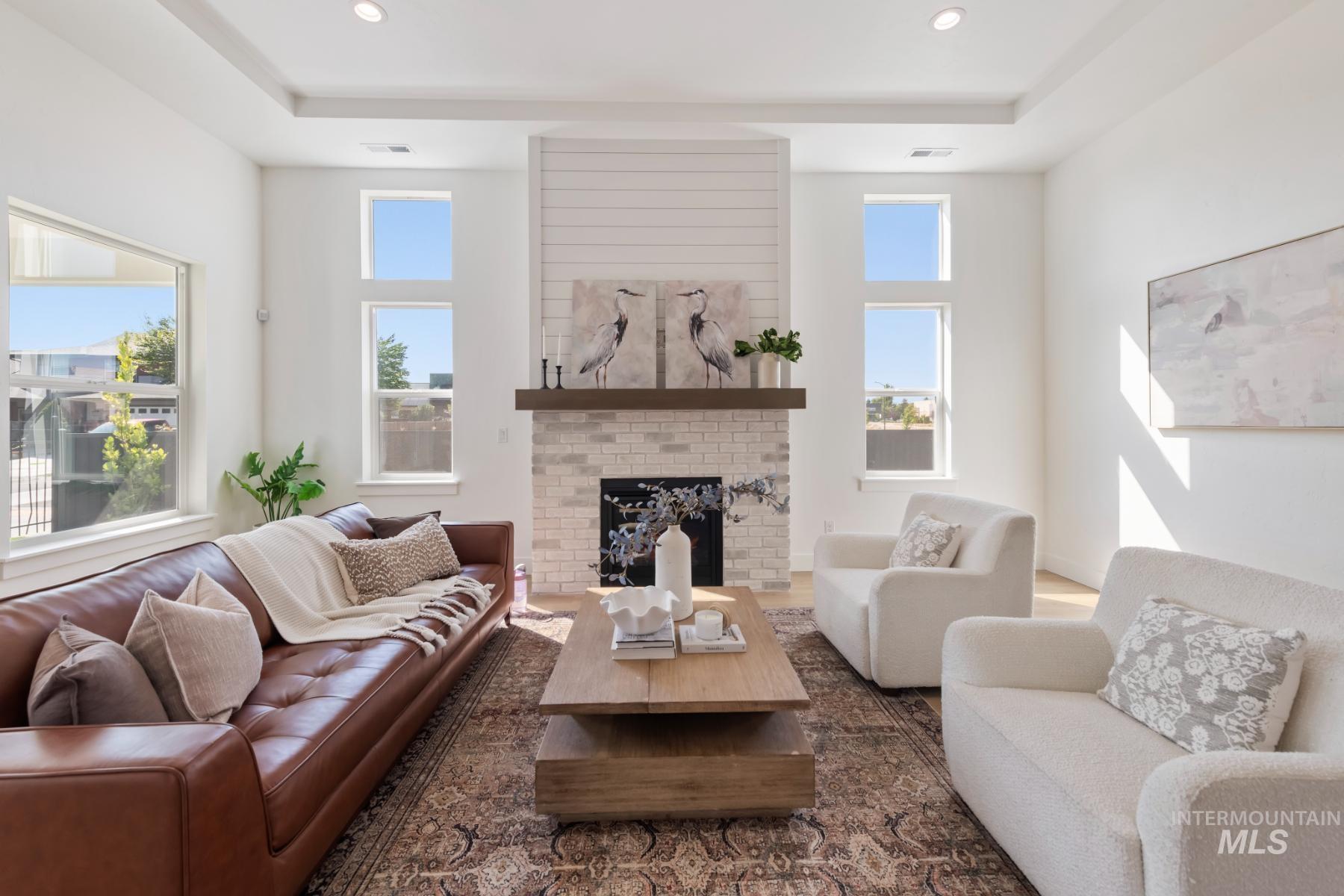 Living room featuring a brick fireplace, wood finished floors, recessed lighting, and a tray ceiling