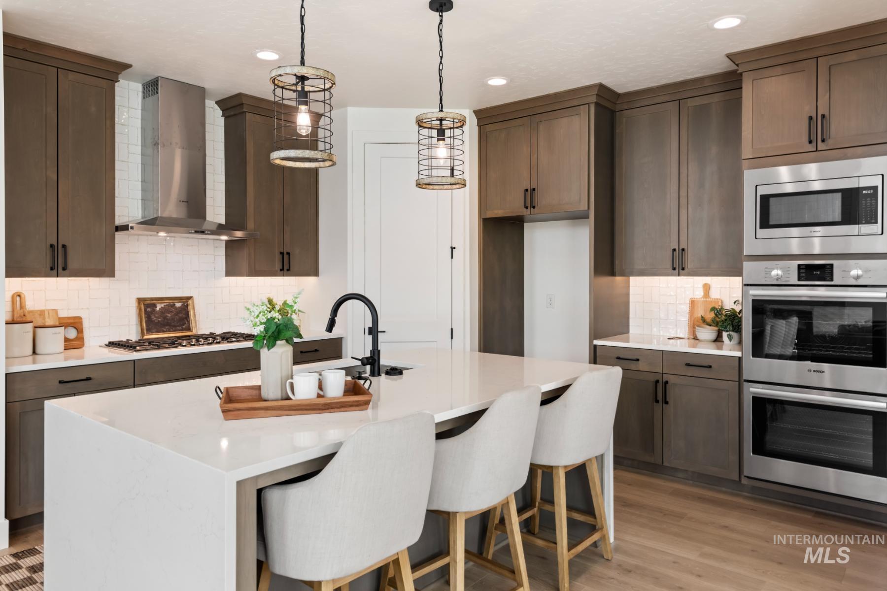 Kitchen featuring decorative backsplash, a breakfast bar area, light stone countertops, stainless steel appliances, and wall chimney range hood