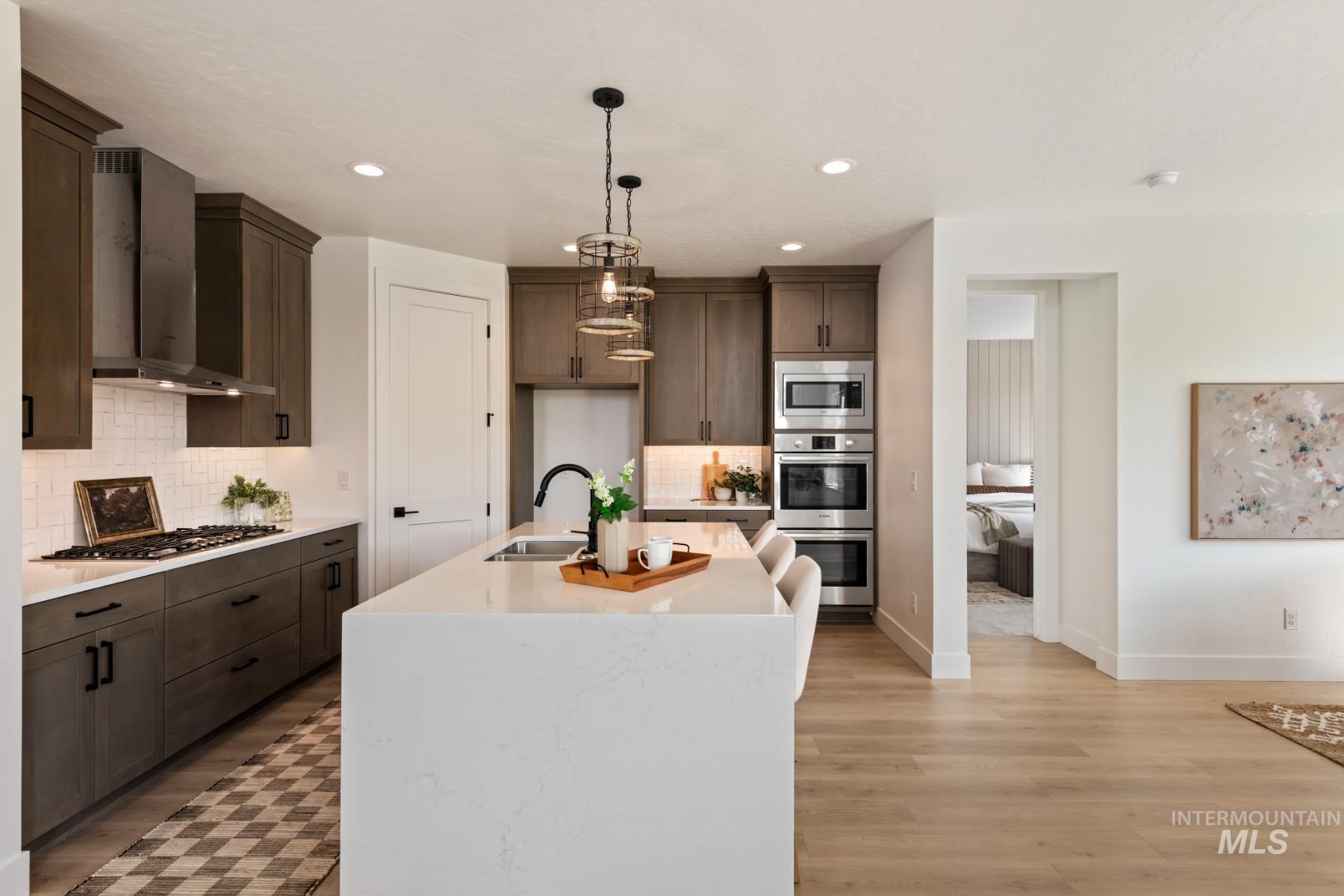Kitchen with light stone countertops, hanging light fixtures, wall chimney exhaust hood, a kitchen island with sink, and backsplash
