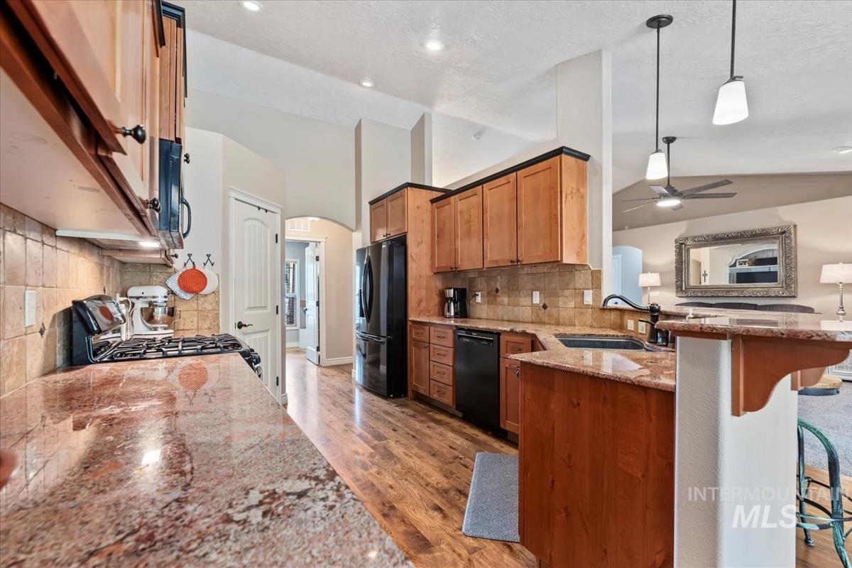 Kitchen with light stone countertops, brown cabinetry, hanging light fixtures, a peninsula, and lofted ceiling