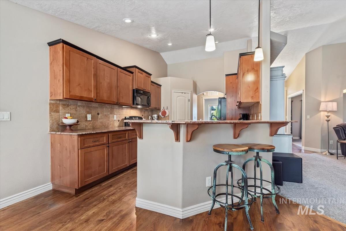 Kitchen with brown cabinets, tasteful backsplash, light stone counters, a kitchen bar, and a peninsula