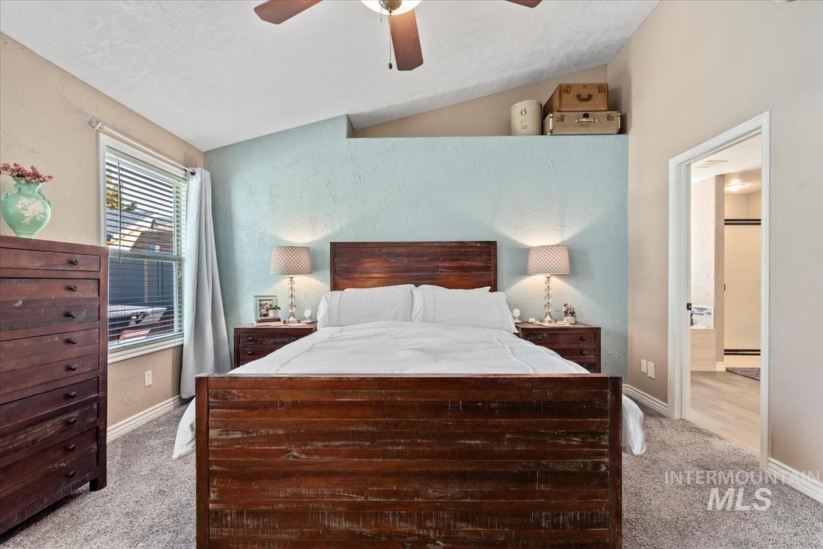 Bedroom featuring light colored carpet, vaulted ceiling, ceiling fan, and a textured wall