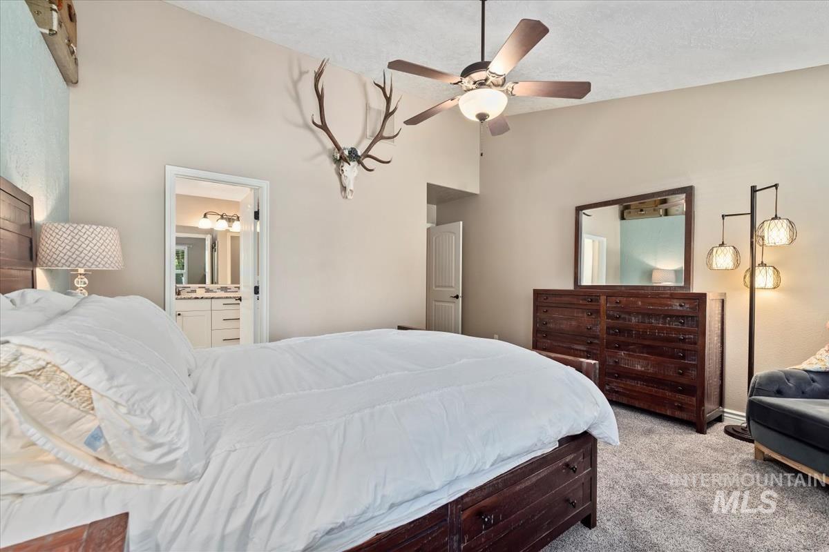 Bedroom with light carpet, a ceiling fan, high vaulted ceiling, and ensuite bath