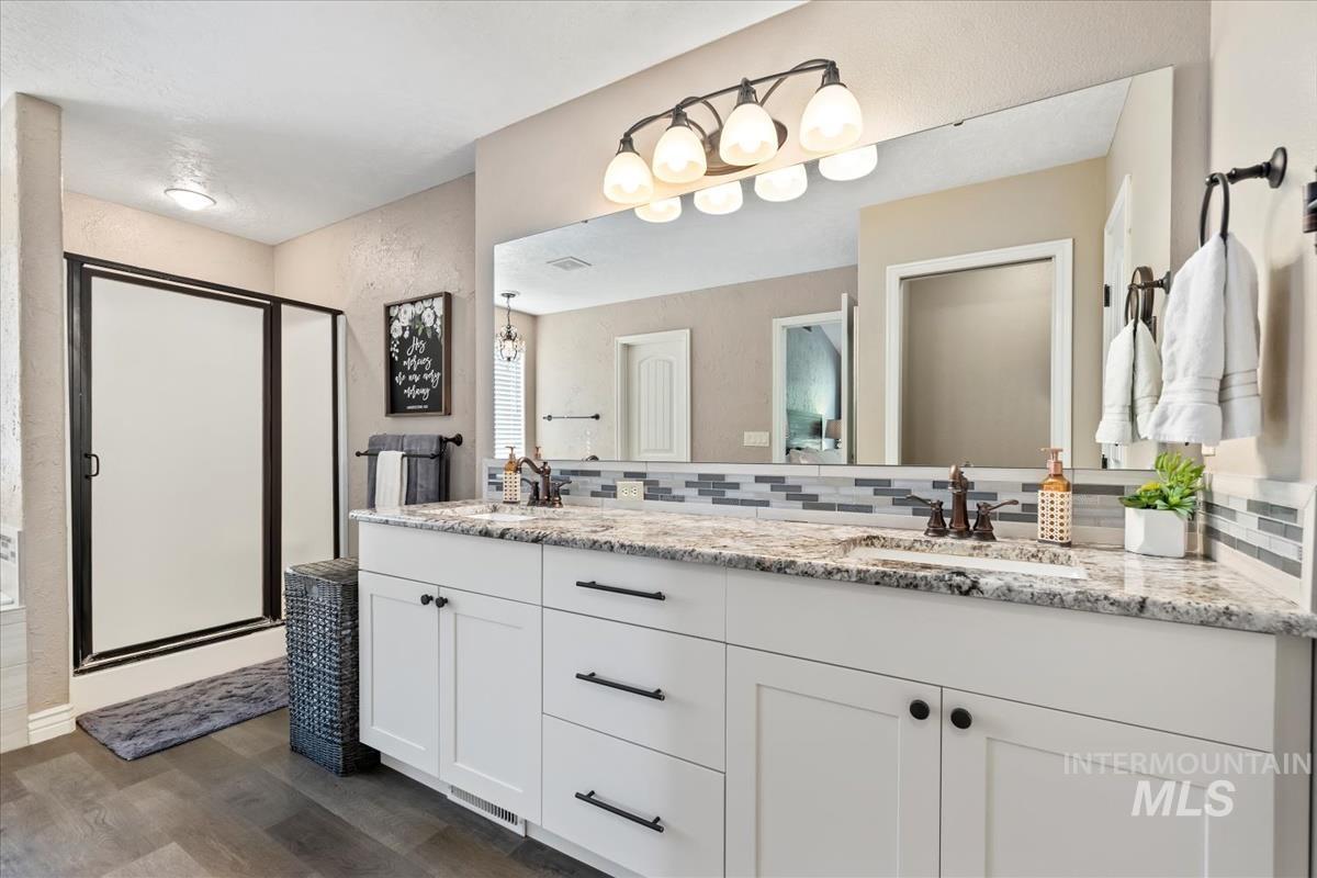 Bathroom featuring dark wood-style floors, a stall shower, double vanity, and decorative backsplash
