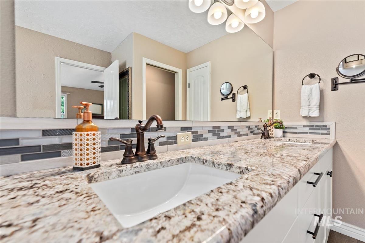 Full bathroom featuring a textured wall, double vanity, and backsplash