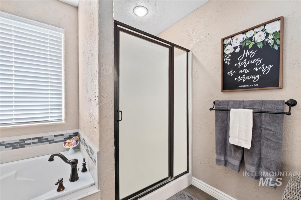 Bathroom featuring a textured wall, a garden tub, and a stall shower