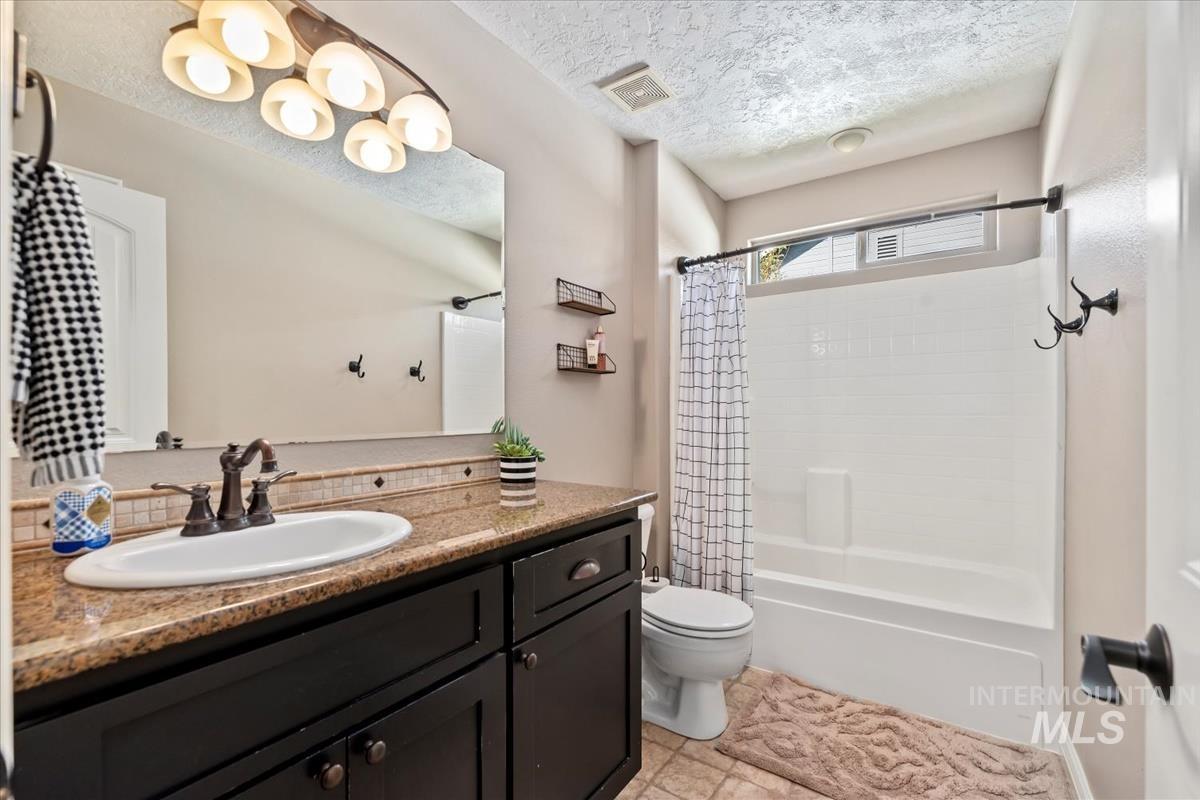 Full bathroom featuring shower / bathtub combination with curtain, a textured ceiling, and vanity