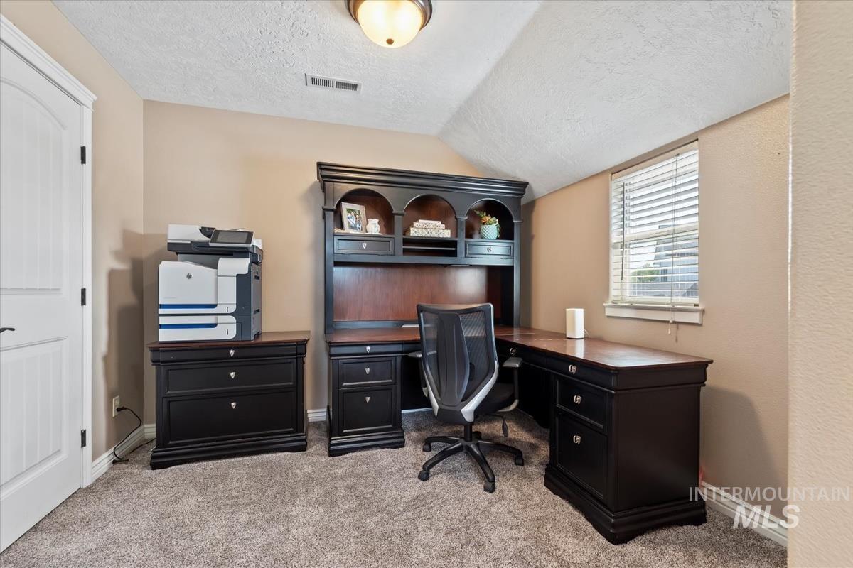 Office space with a textured ceiling, light carpet, and vaulted ceiling