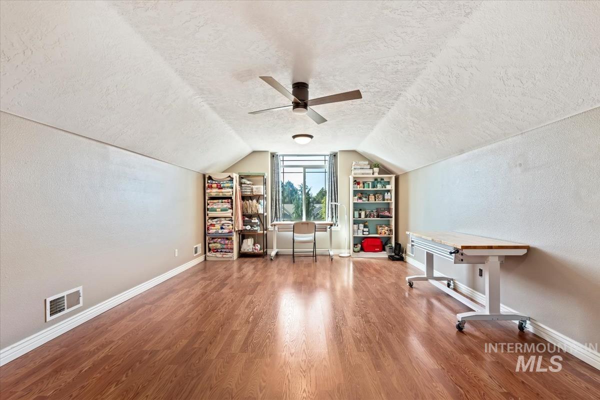 Unfurnished office featuring a textured ceiling, a textured wall, wood finished floors, vaulted ceiling, and ceiling fan