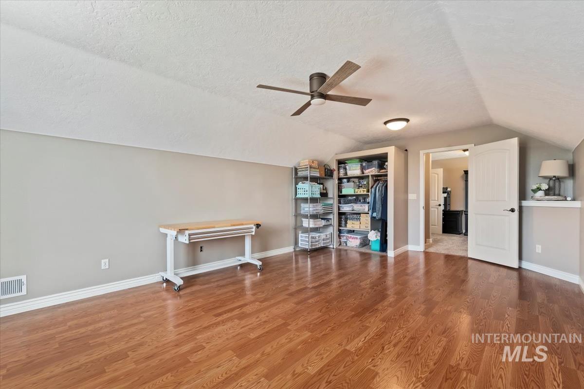 Additional living space with a textured ceiling, lofted ceiling, wood finished floors, and ceiling fan