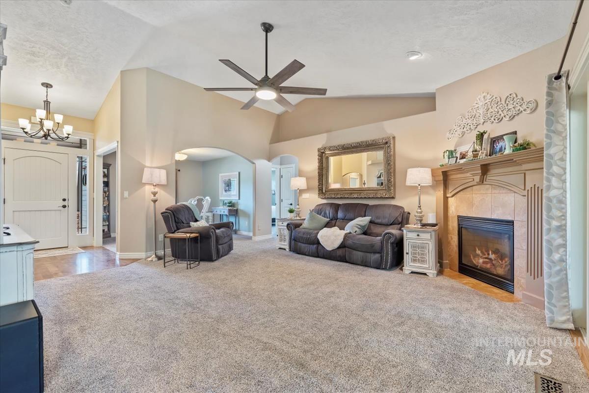 Living area featuring vaulted ceiling, light carpet, ceiling fan, a tiled fireplace, and a chandelier