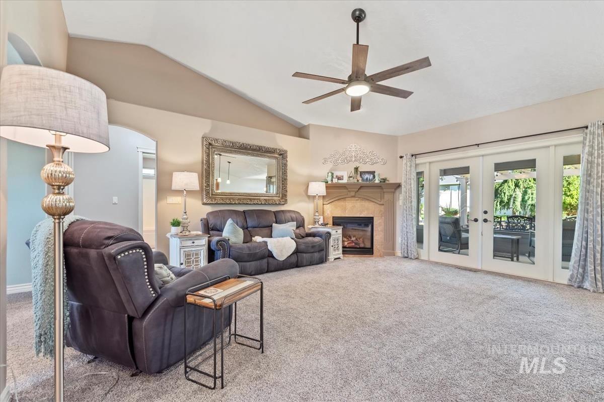 Living room with lofted ceiling, carpet flooring, french doors, a glass covered fireplace, and a ceiling fan