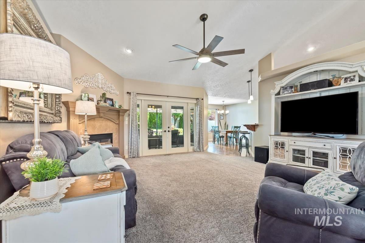Carpeted living room featuring a glass covered fireplace, lofted ceiling, french doors, ceiling fan, and a chandelier