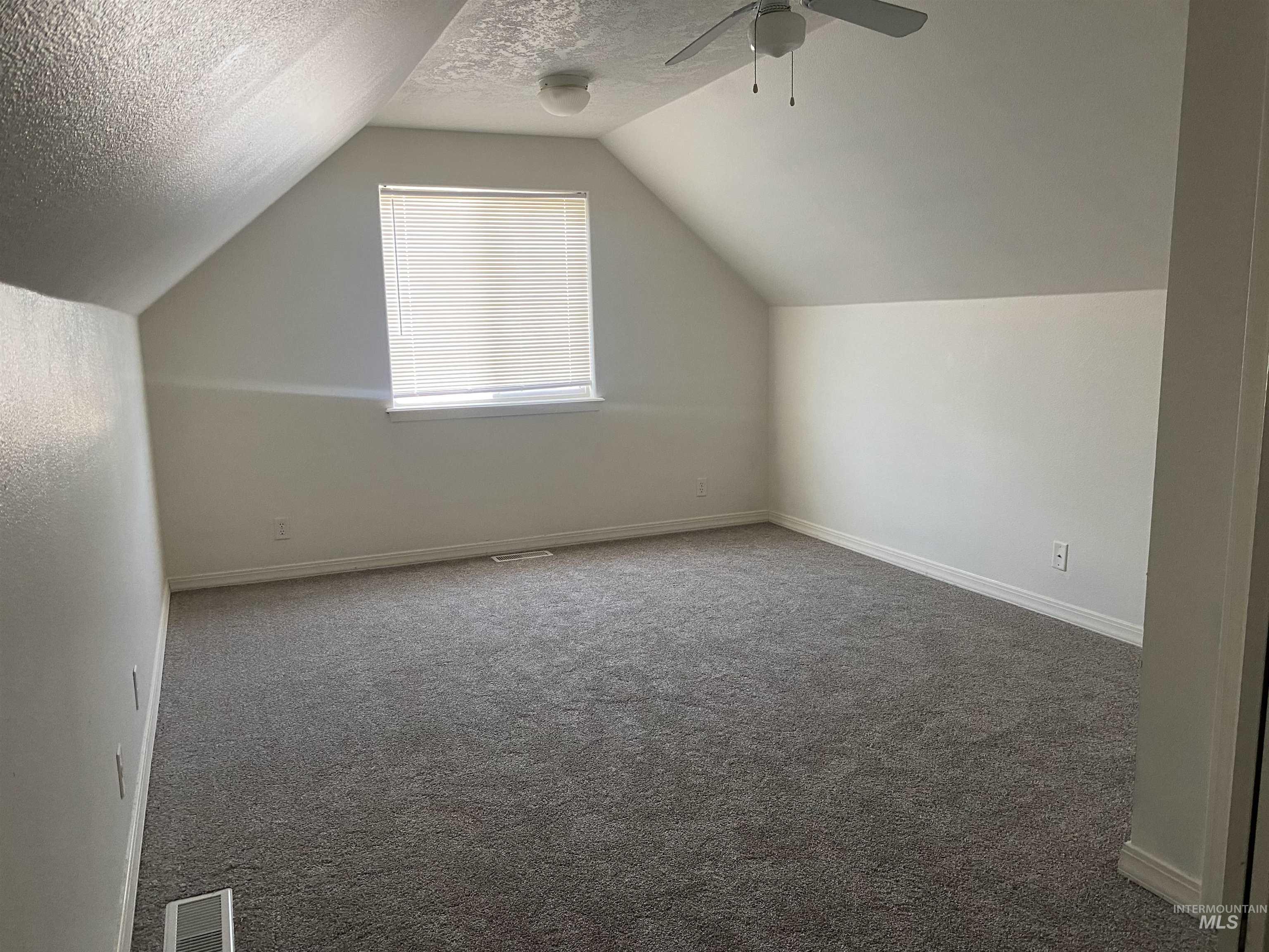 Additional living space with carpet floors, vaulted ceiling, a textured ceiling, and ceiling fan