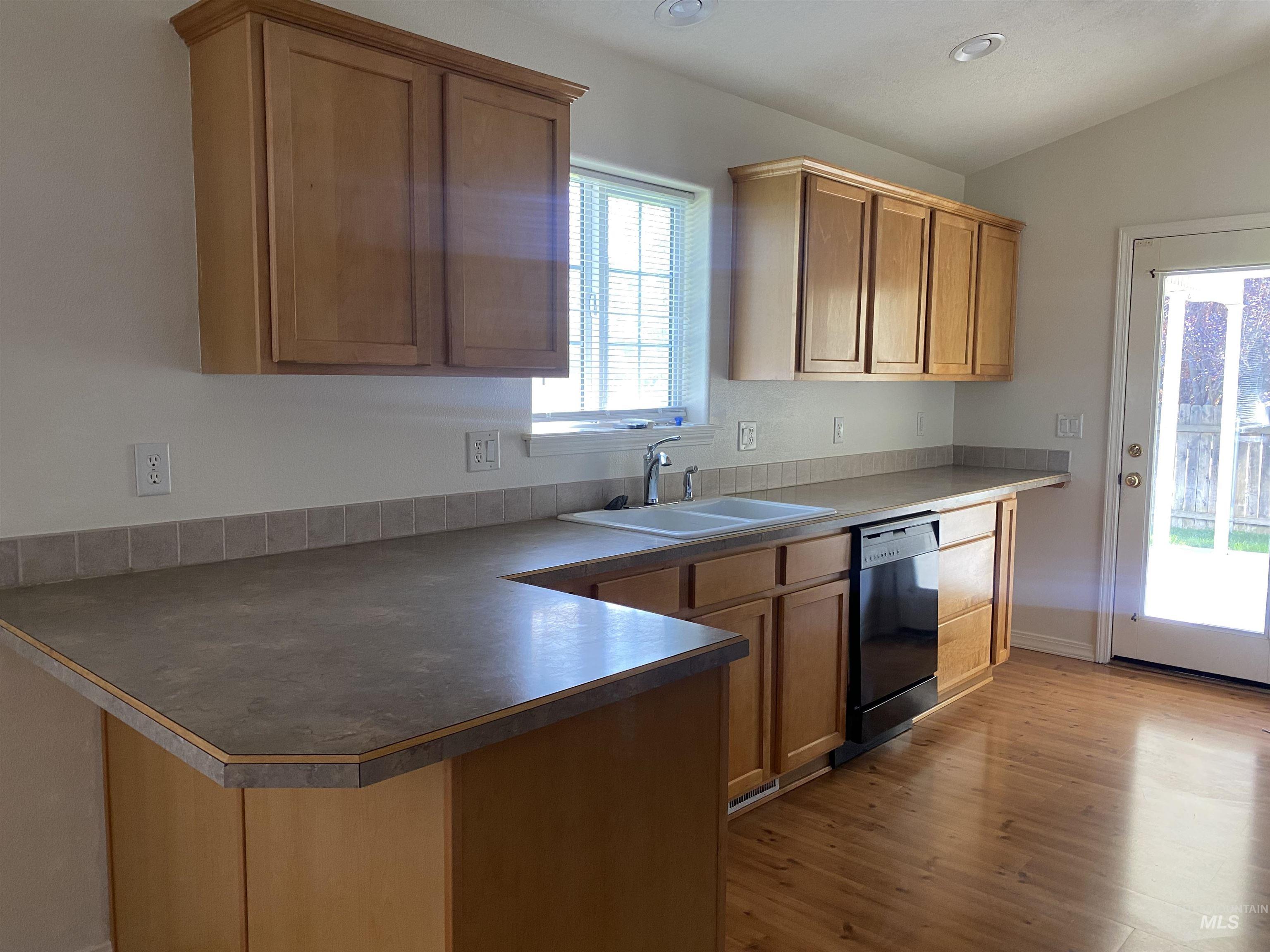 Kitchen with a peninsula, dark countertops, black dishwasher, dark wood-style flooring, and a kitchen bar