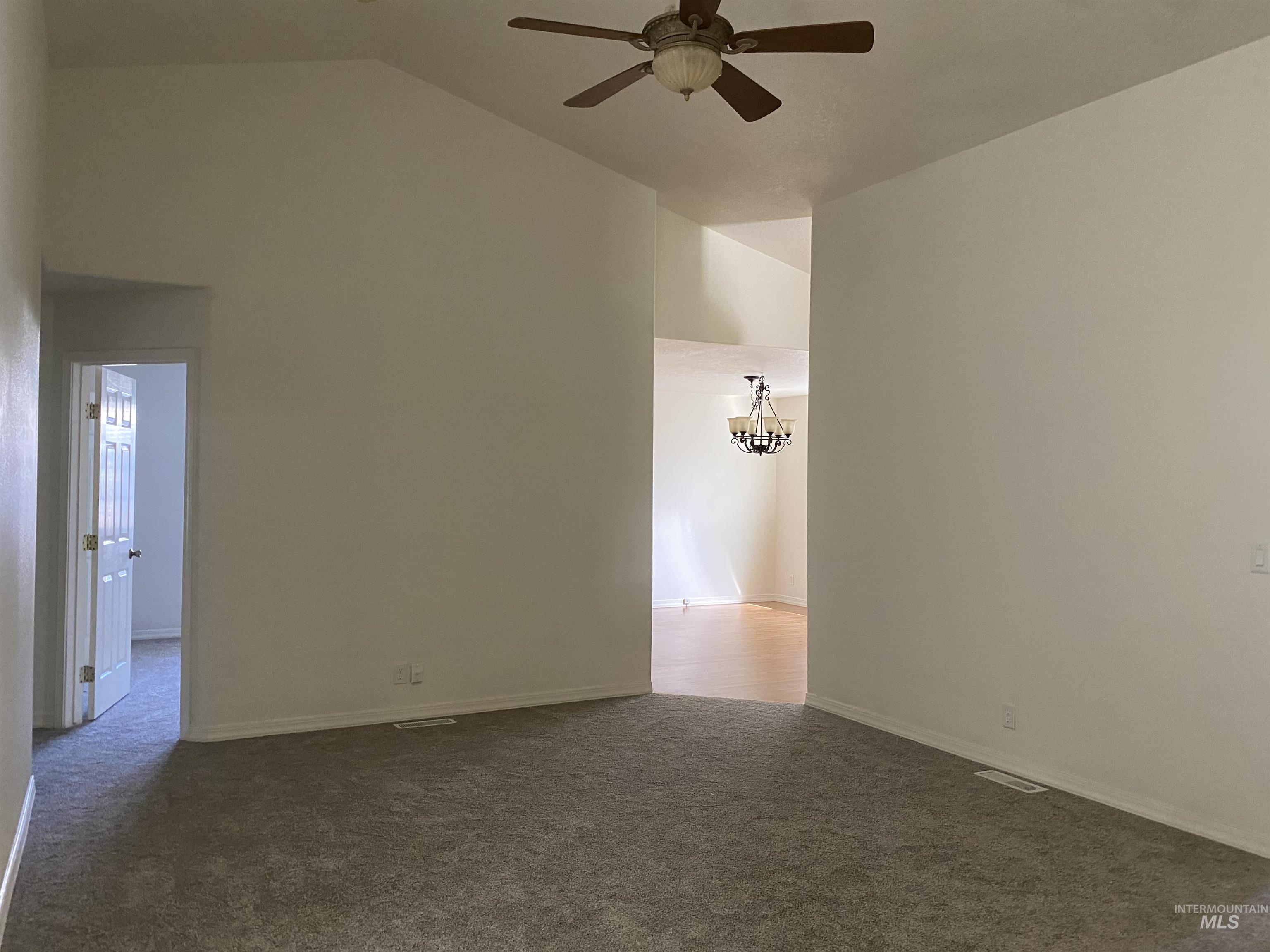 Spare room featuring dark colored carpet, high vaulted ceiling, a chandelier, and a ceiling fan