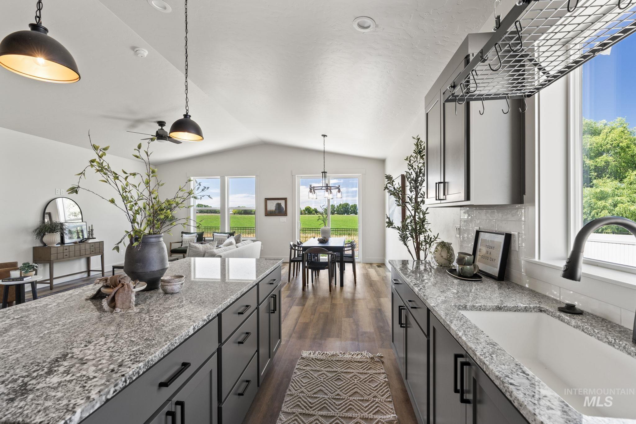 Kitchen with hanging light fixtures, light stone countertops, gray cabinetry, and vaulted ceiling