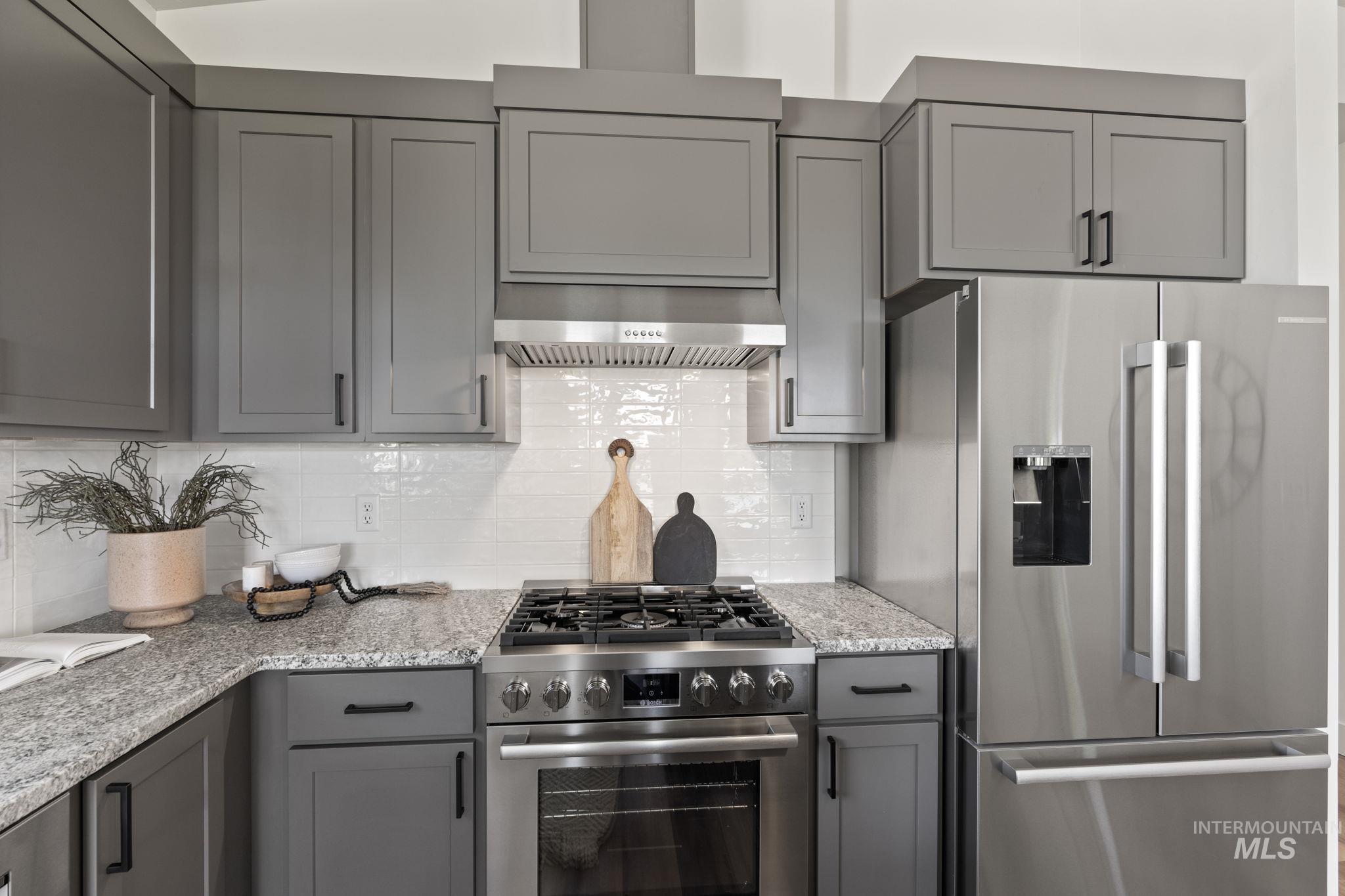 Kitchen with gray cabinets, appliances with stainless steel finishes, tasteful backsplash, and light stone countertops