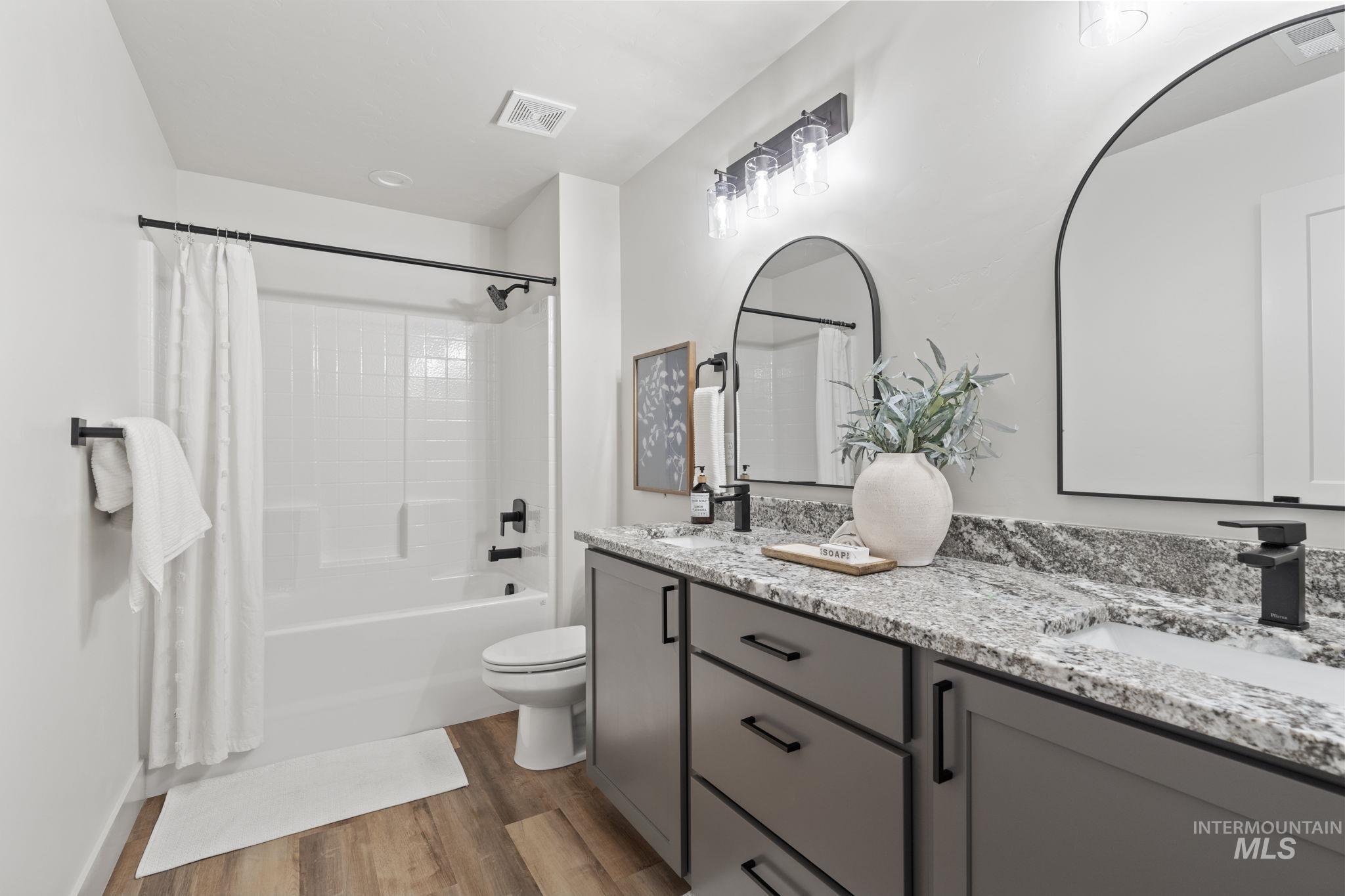 Full bath with shower / tub combo, double vanity, and light wood-style flooring