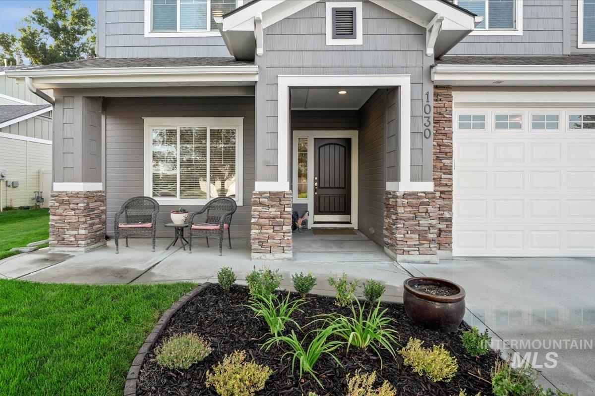 Doorway to property with stone siding, covered porch, a shingled roof, and a garage