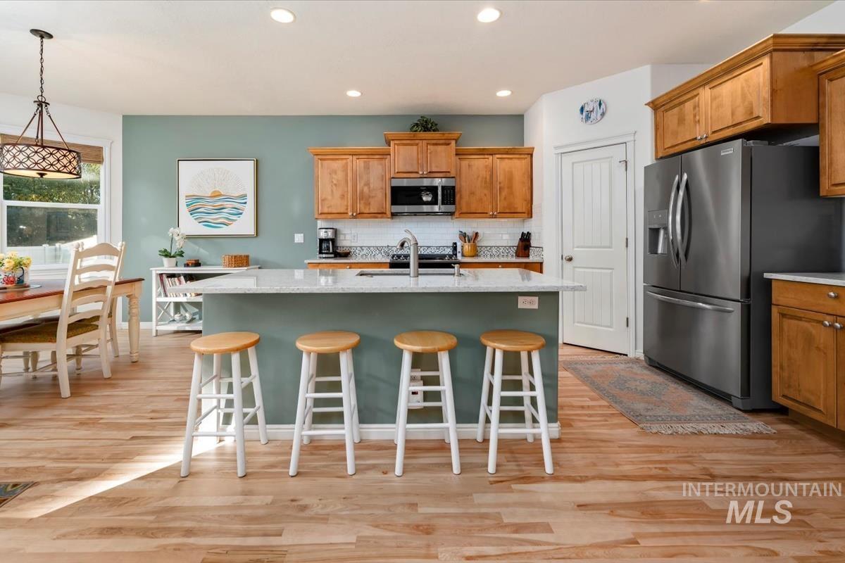 Kitchen with tasteful backsplash, appliances with stainless steel finishes, a breakfast bar area, light wood-style flooring, and light stone countertops