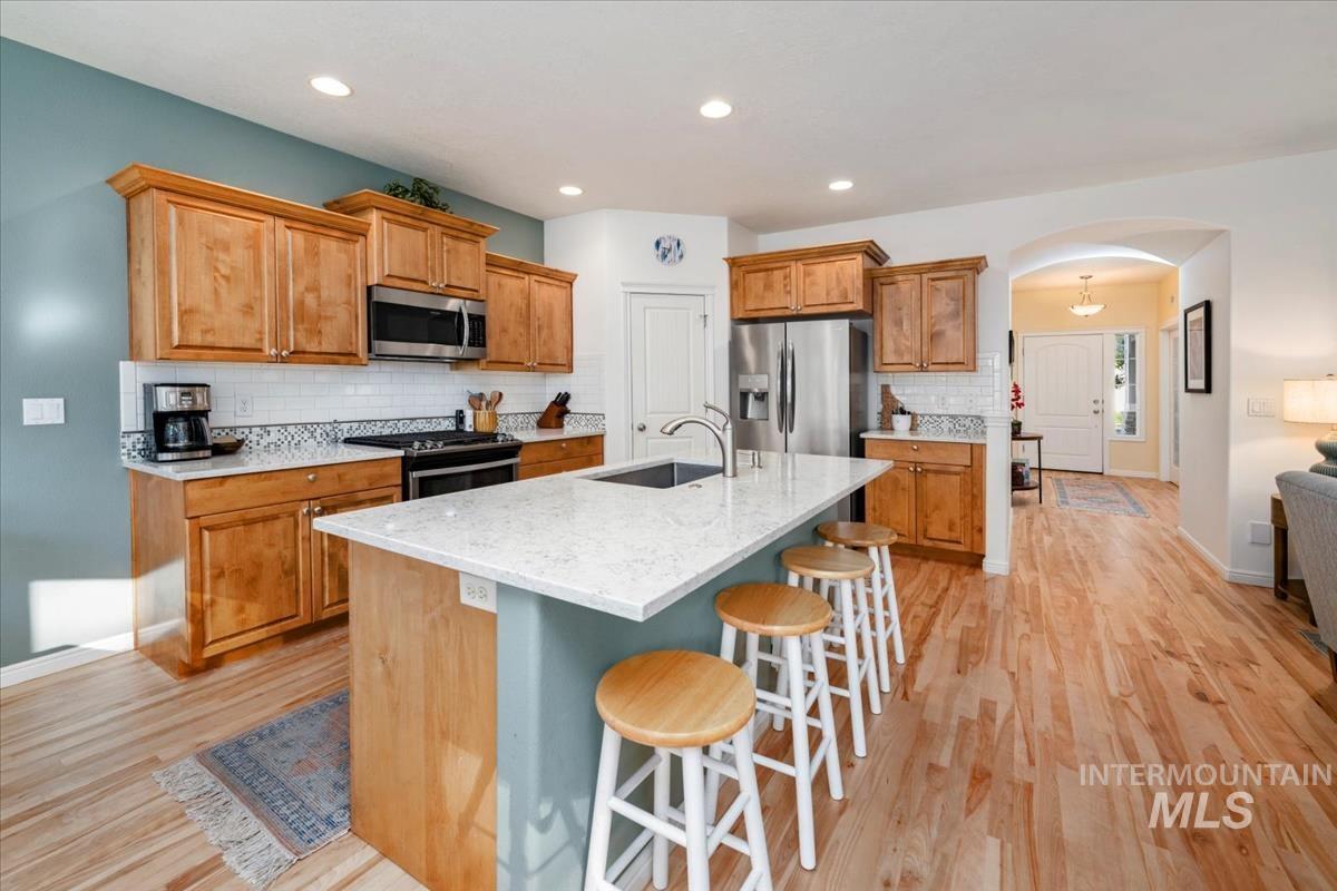 Kitchen with arched walkways, tasteful backsplash, appliances with stainless steel finishes, light stone counters, and a breakfast bar
