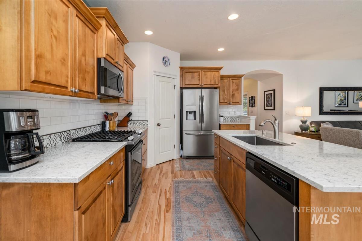 Kitchen with appliances with stainless steel finishes, light wood finished floors, arched walkways, light stone counters, and decorative backsplash