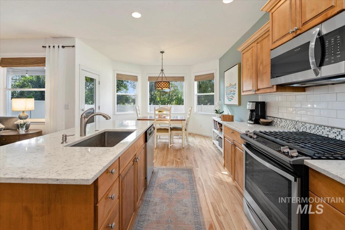 Kitchen with appliances with stainless steel finishes, light stone counters, light wood-style floors, brown cabinets, and recessed lighting