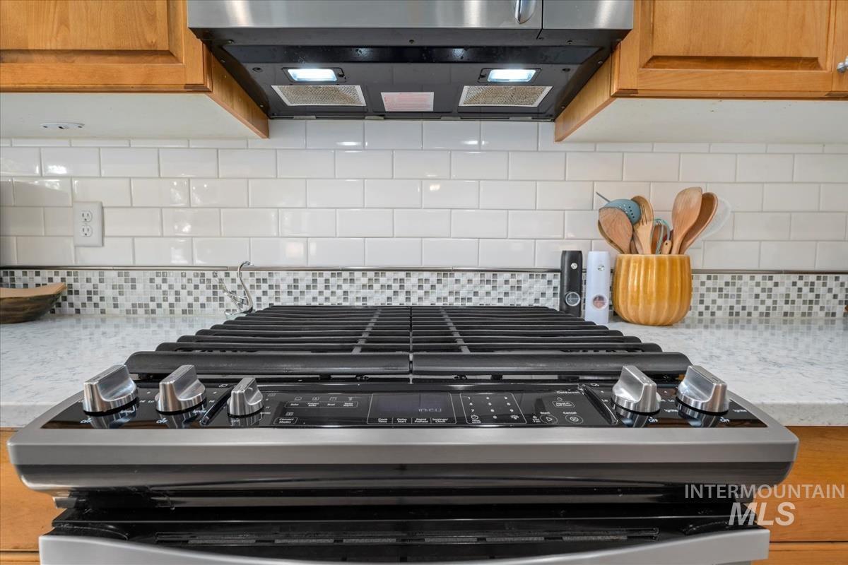 Kitchen view of backsplash, extractor fan, gas range, and light stone counters