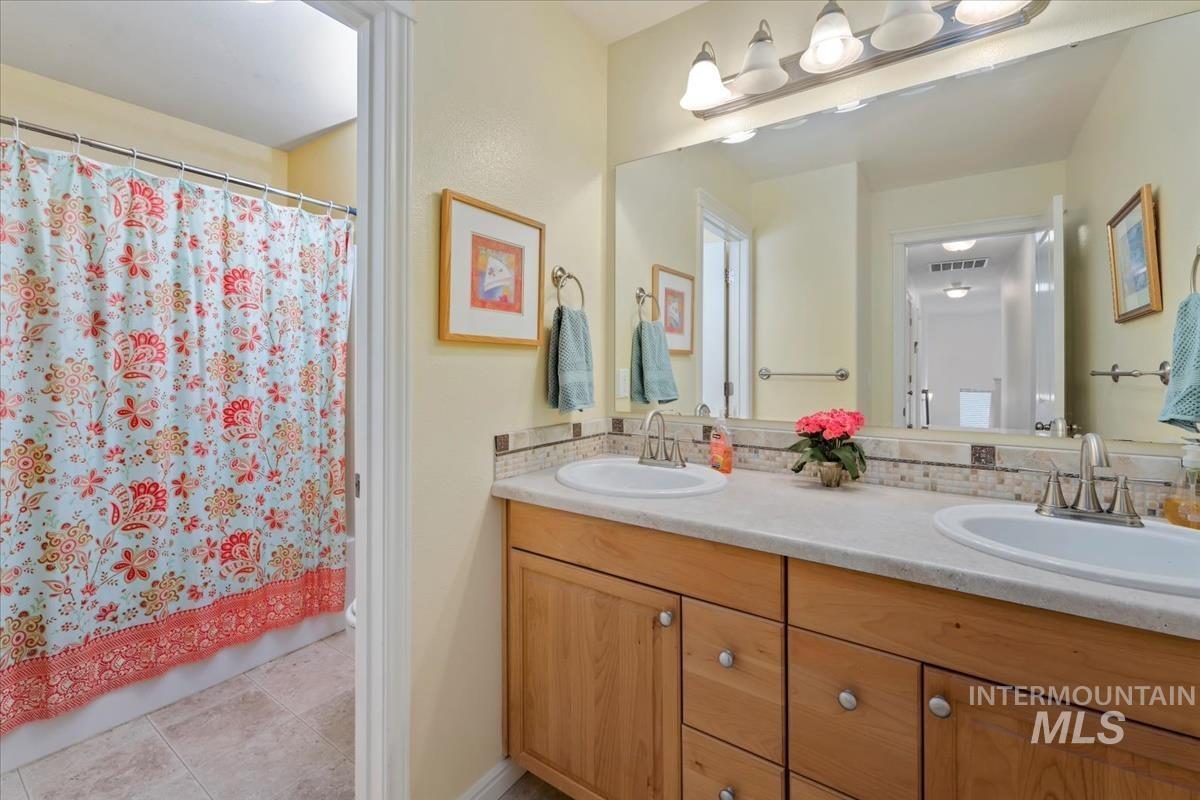 Bathroom featuring double vanity, light tile patterned floors, and shower / tub combo with curtain