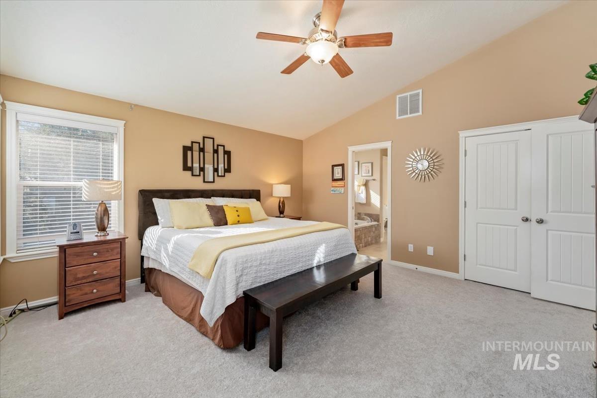 Bedroom with light carpet, ceiling fan, ensuite bath, and high vaulted ceiling