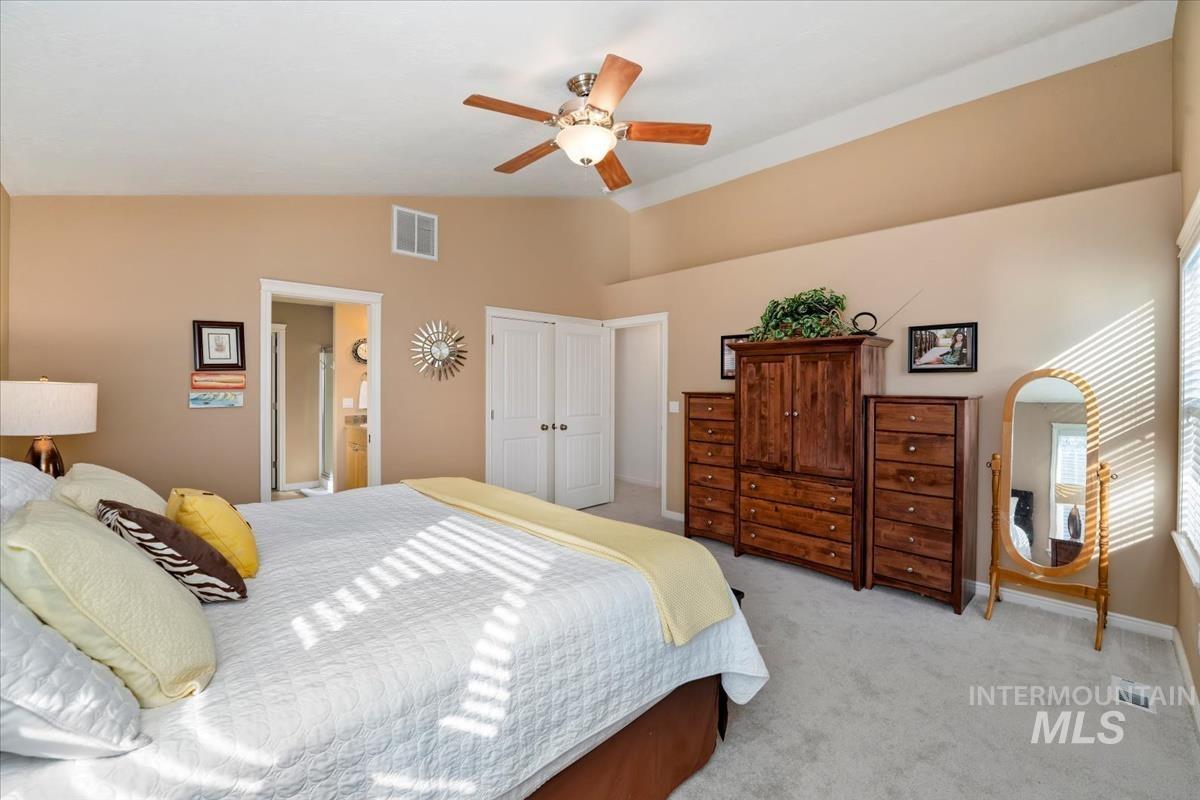 Carpeted bedroom featuring vaulted ceiling, a ceiling fan, ensuite bath, and a closet