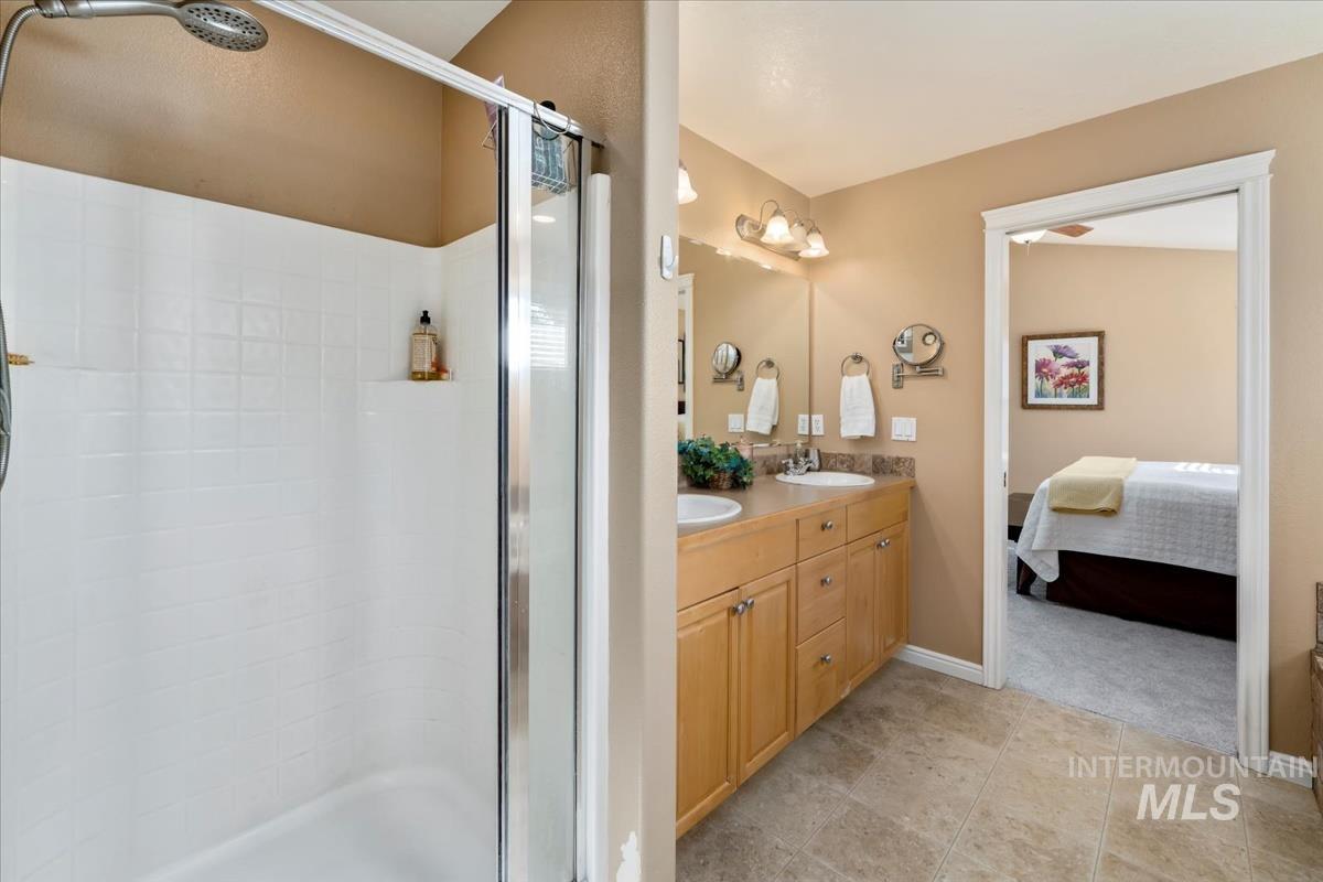 Ensuite bathroom with a shower stall, double vanity, and light tile patterned flooring