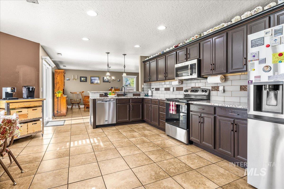 Kitchen with stainless steel appliances, pendant lighting, a textured ceiling, dark brown cabinetry, and light tile patterned flooring